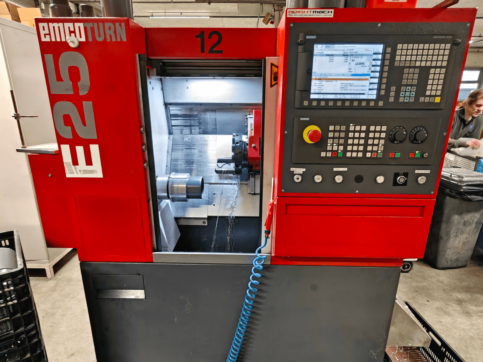 Vista frontal da máquina EMCO TURN E25, com painel de controlo, suporte da ferramenta e área interior com a ferramenta de corte visível.