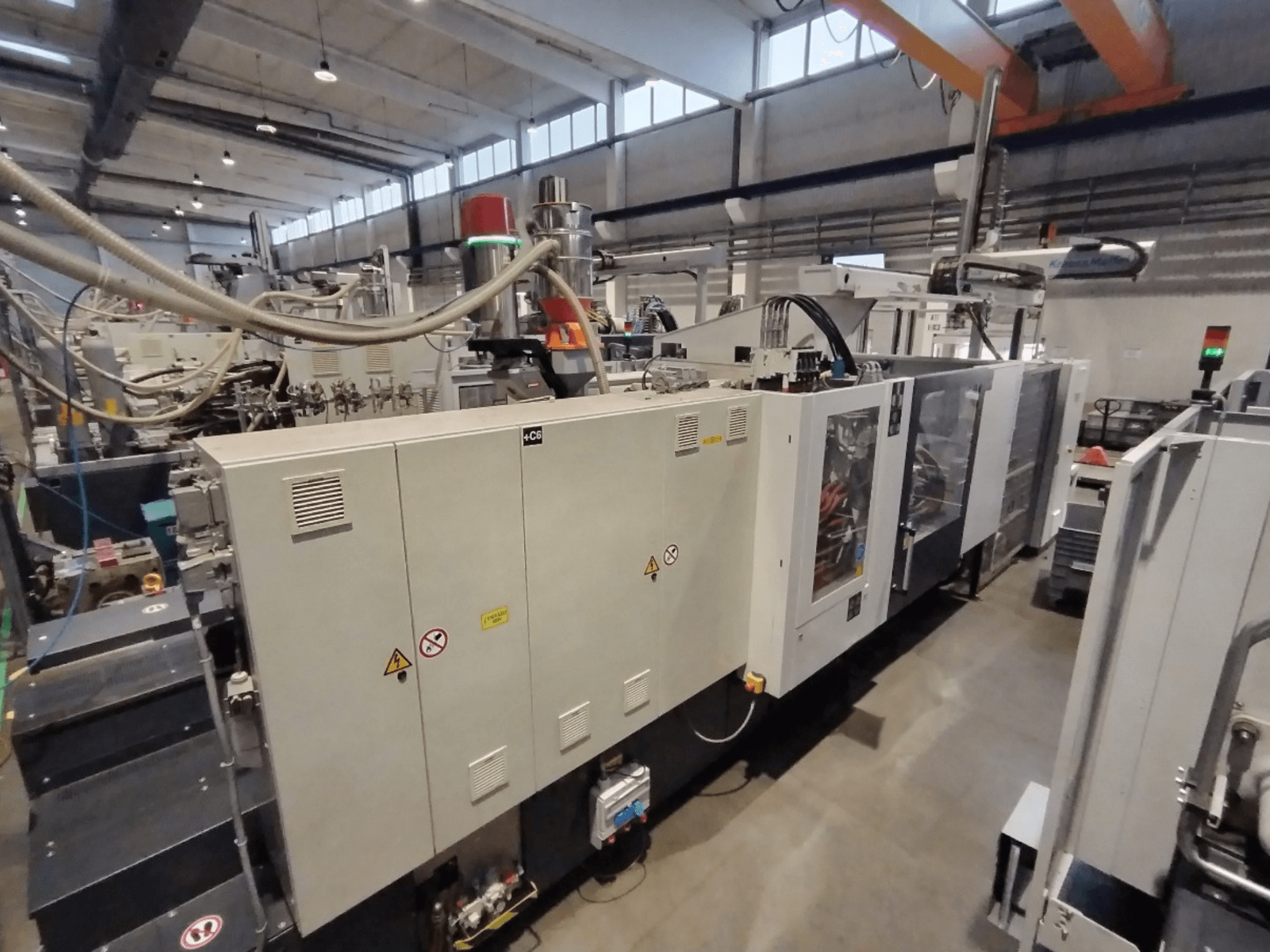 Máquina de moldagem por injeção industrial vista de lado, com painel de controlo e avisos de segurança. Marca: Desconhecida.