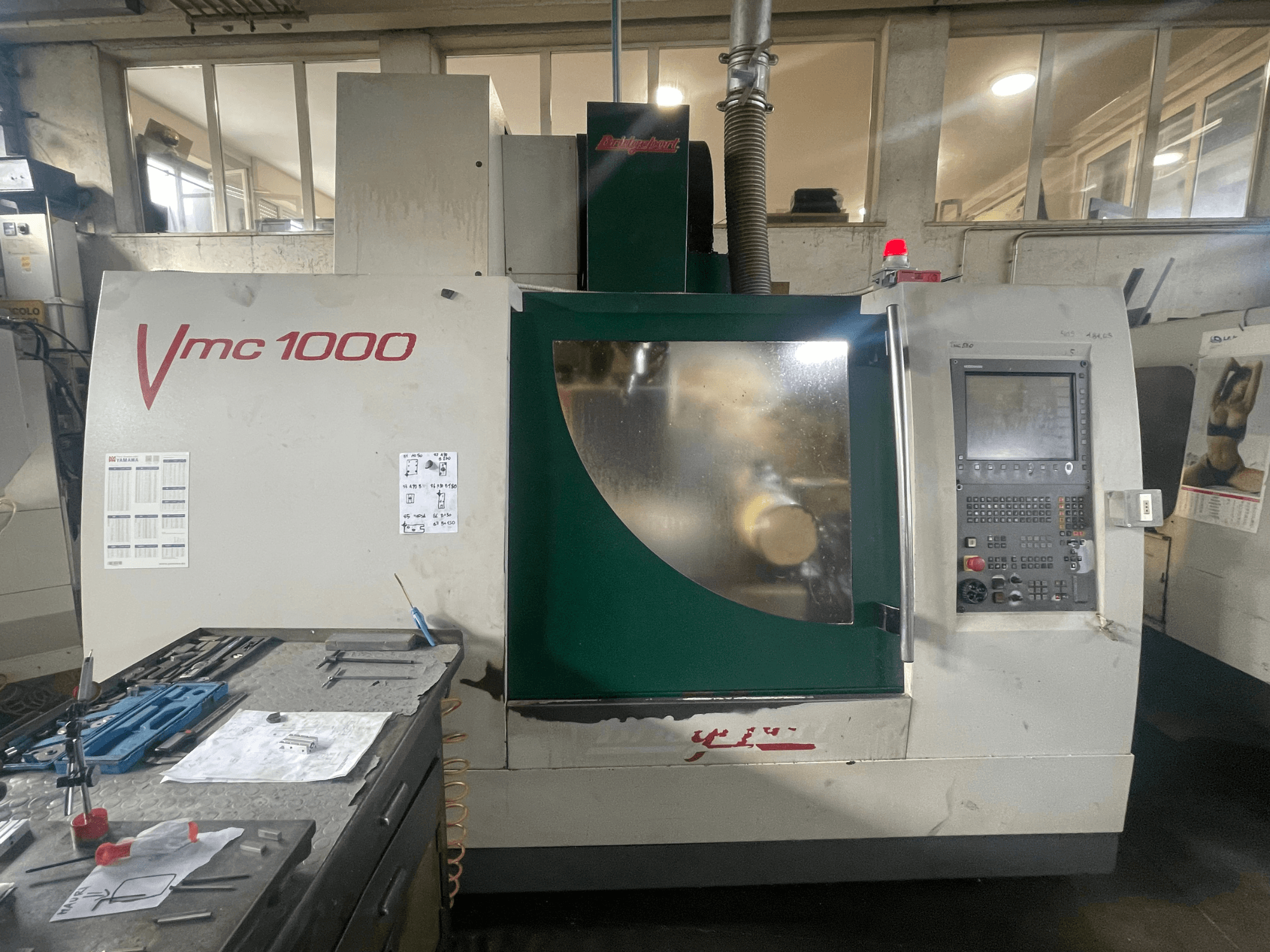 Centro de maquinagem vertical Bridgeport VMC 1000/30, vista frontal, mostrando o painel de controlo e o corpo principal, com ferramentas nas proximidades.