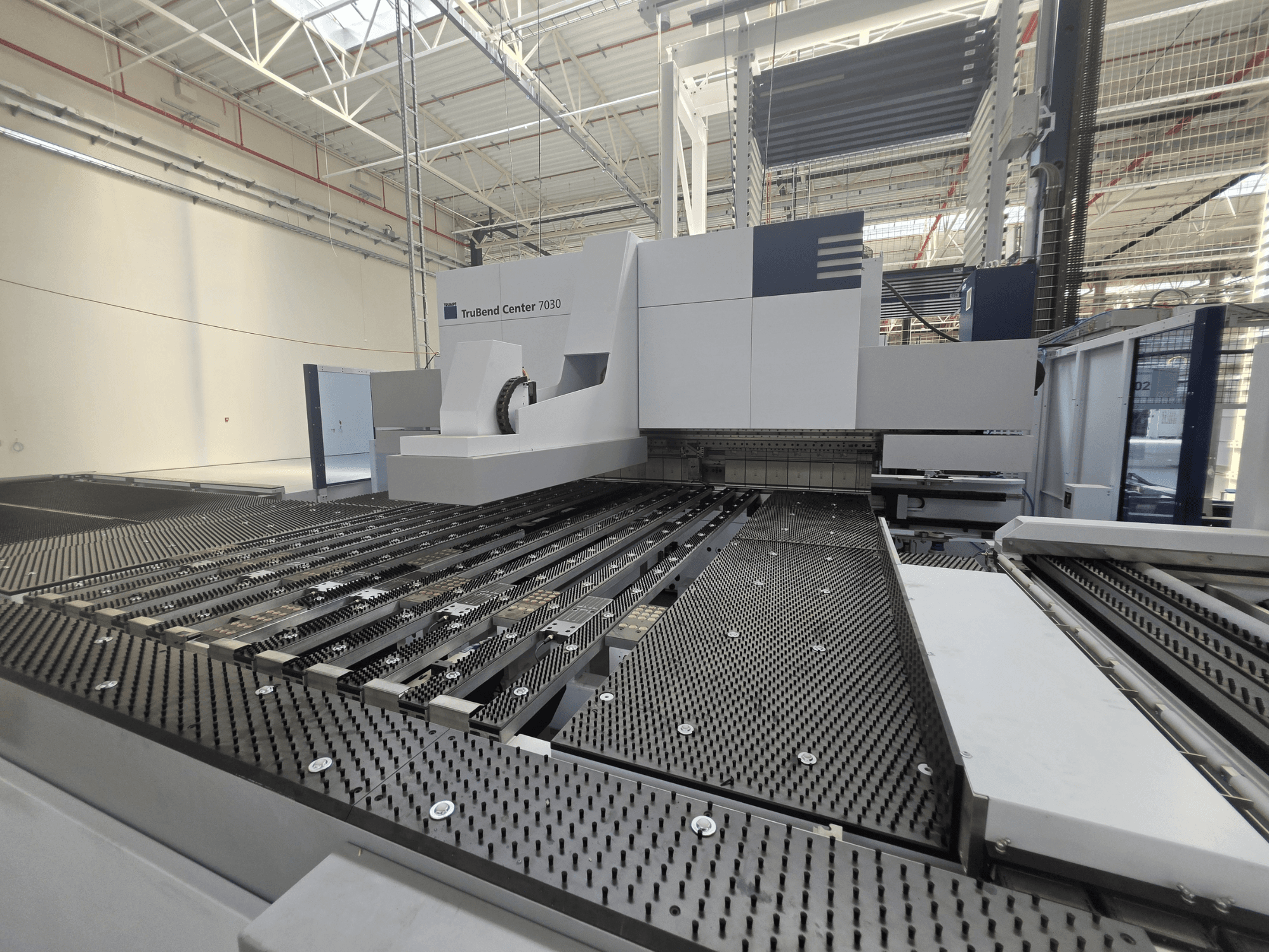 Máquina de dobragem TRUMPF TruBend Center 7030 num ambiente fabril, vista frontal que mostra a mesa de trabalho complexa e o braço de dobragem.