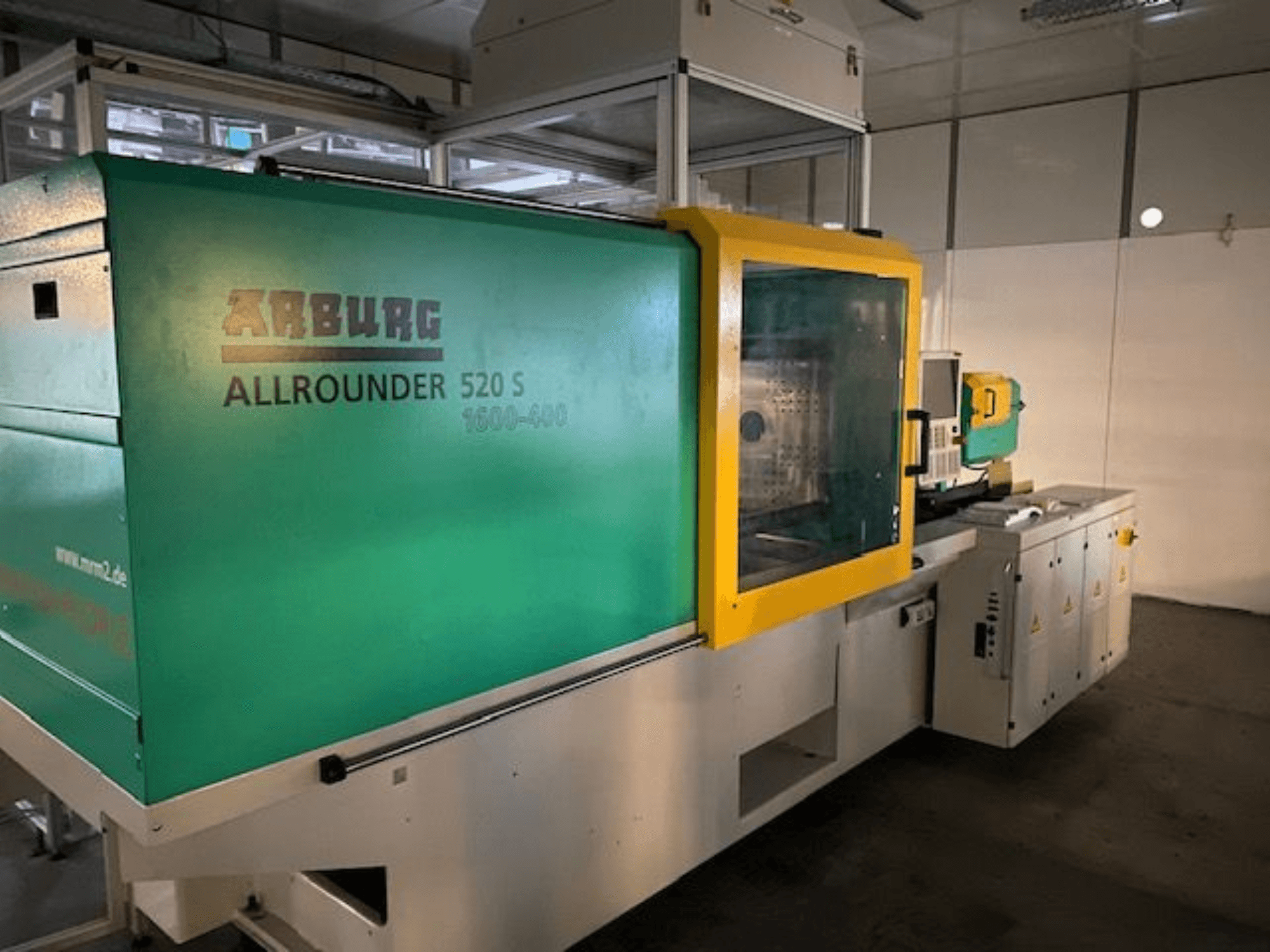 Máquina de moldagem por injeção Arburg Allrounder 520 S, vista lateral, com um exterior verde e amarelo, detalhes técnicos visíveis.