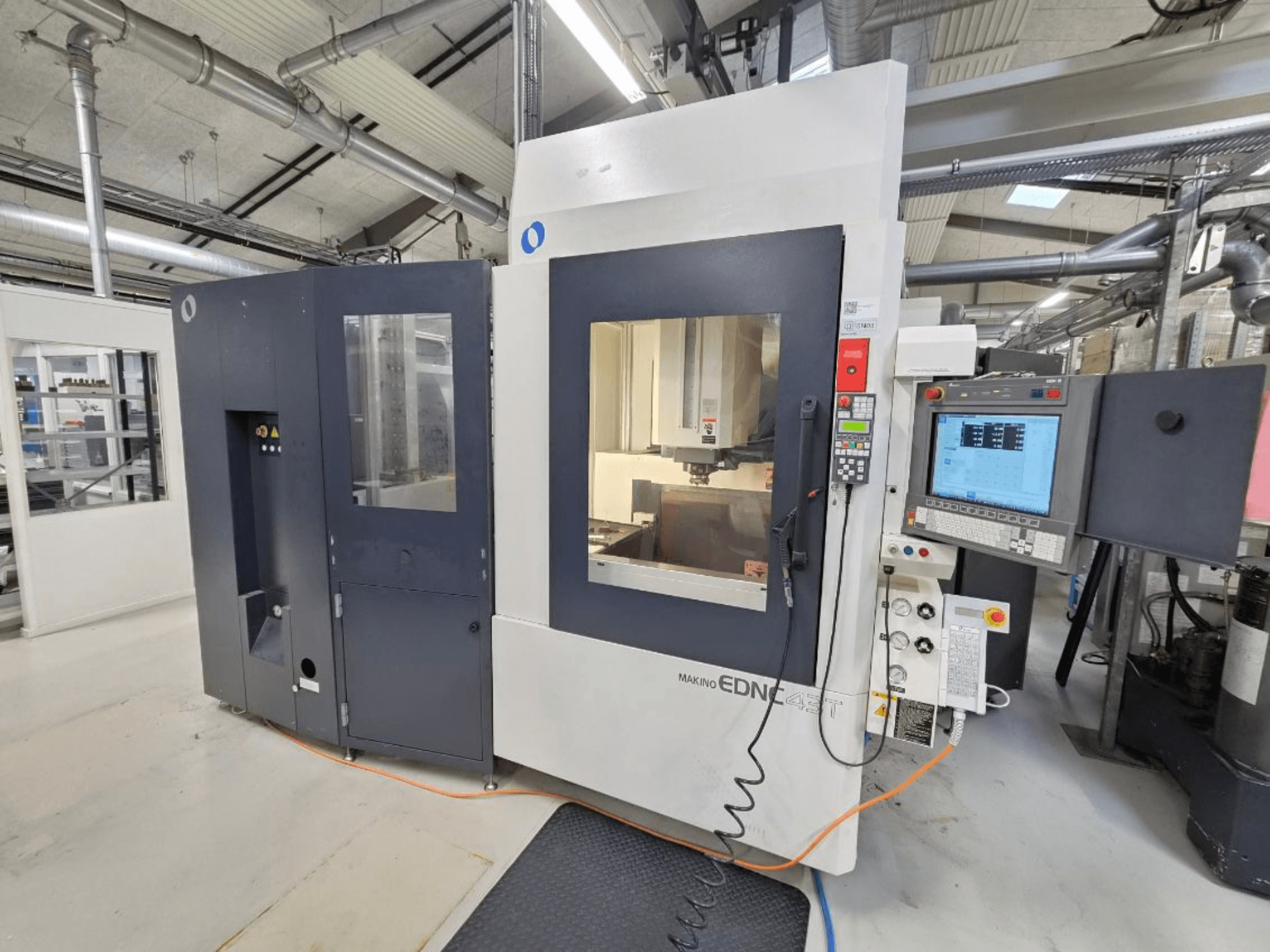 Vista frontal de uma máquina de eletroerosão por penetração Makino EDNC 43T, com o robô Erowa, os comandos e a área de trabalho visível.