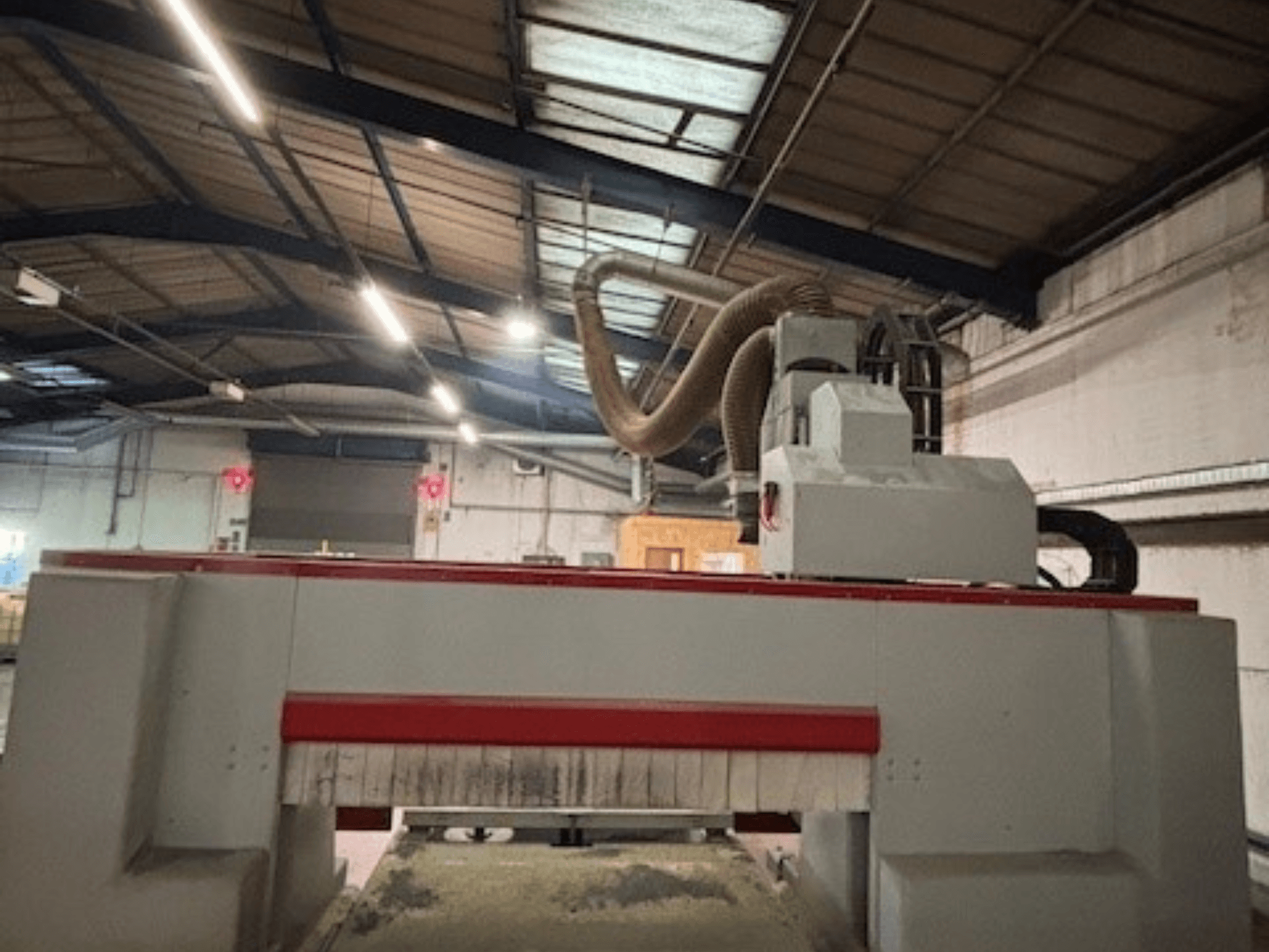 Máquina de fresar CNC numa oficina, vista lateral destacando o design vermelho e cinzento, sistema de extração de poeiras anexado.