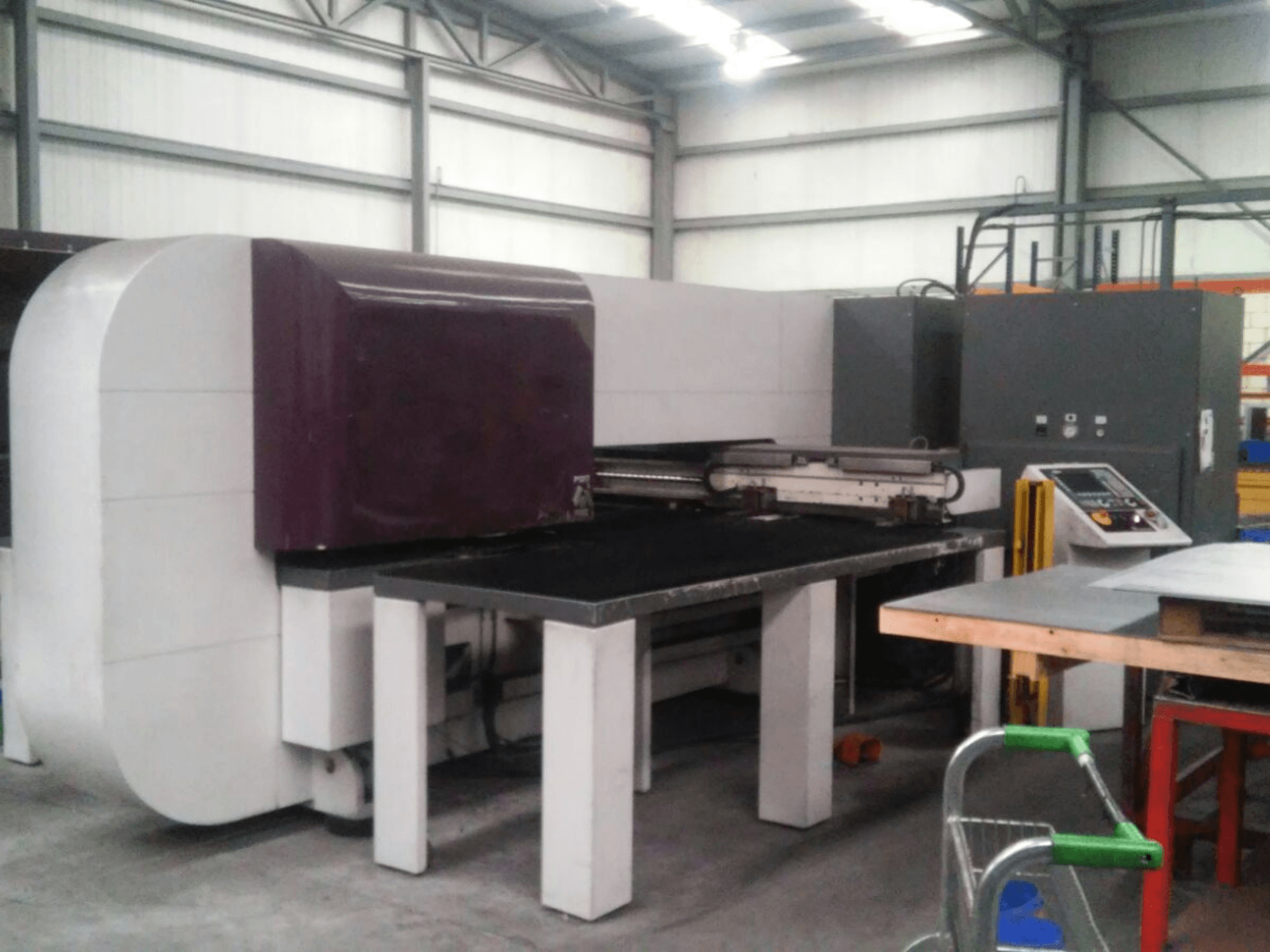 Máquina industrial roxa com uma superfície plana, vista lateral, com comandos e uma base robusta para tarefas operacionais.
