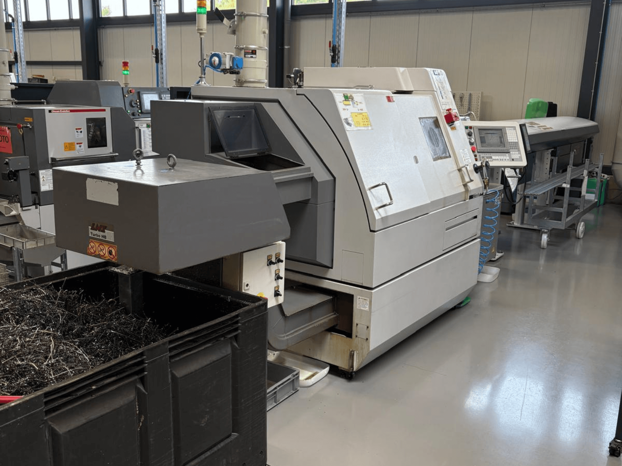 Máquina industrial LTA Turbo H8, vista lateral, com um grande recipiente para aparas de metal e painel de controlo numa fábrica.