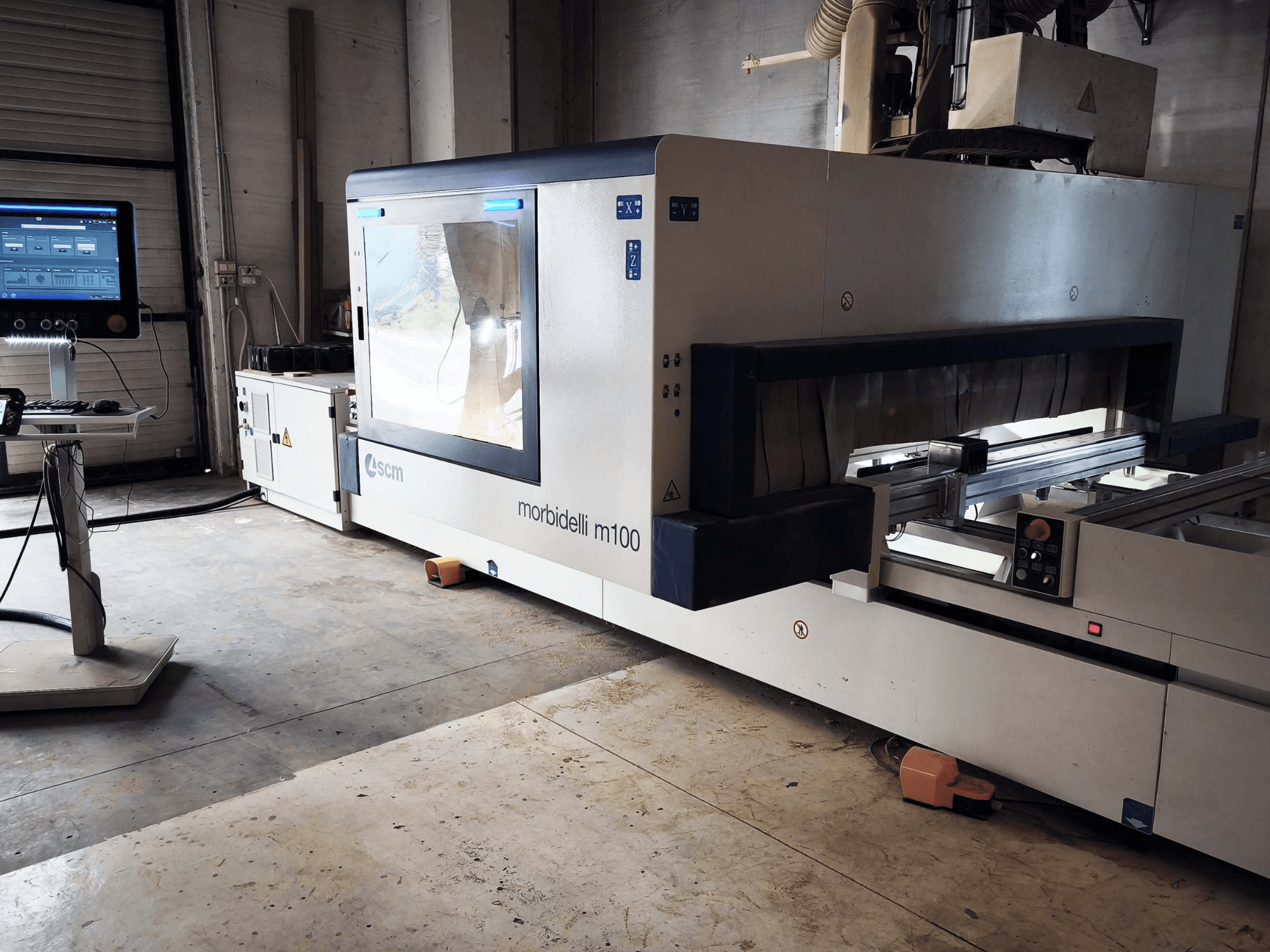 Centro de usinagem de madeira CNC SCM Morbidelli M 100, visto de lado, mostrando o painel de controlo, a área de trabalho e as características de segurança.