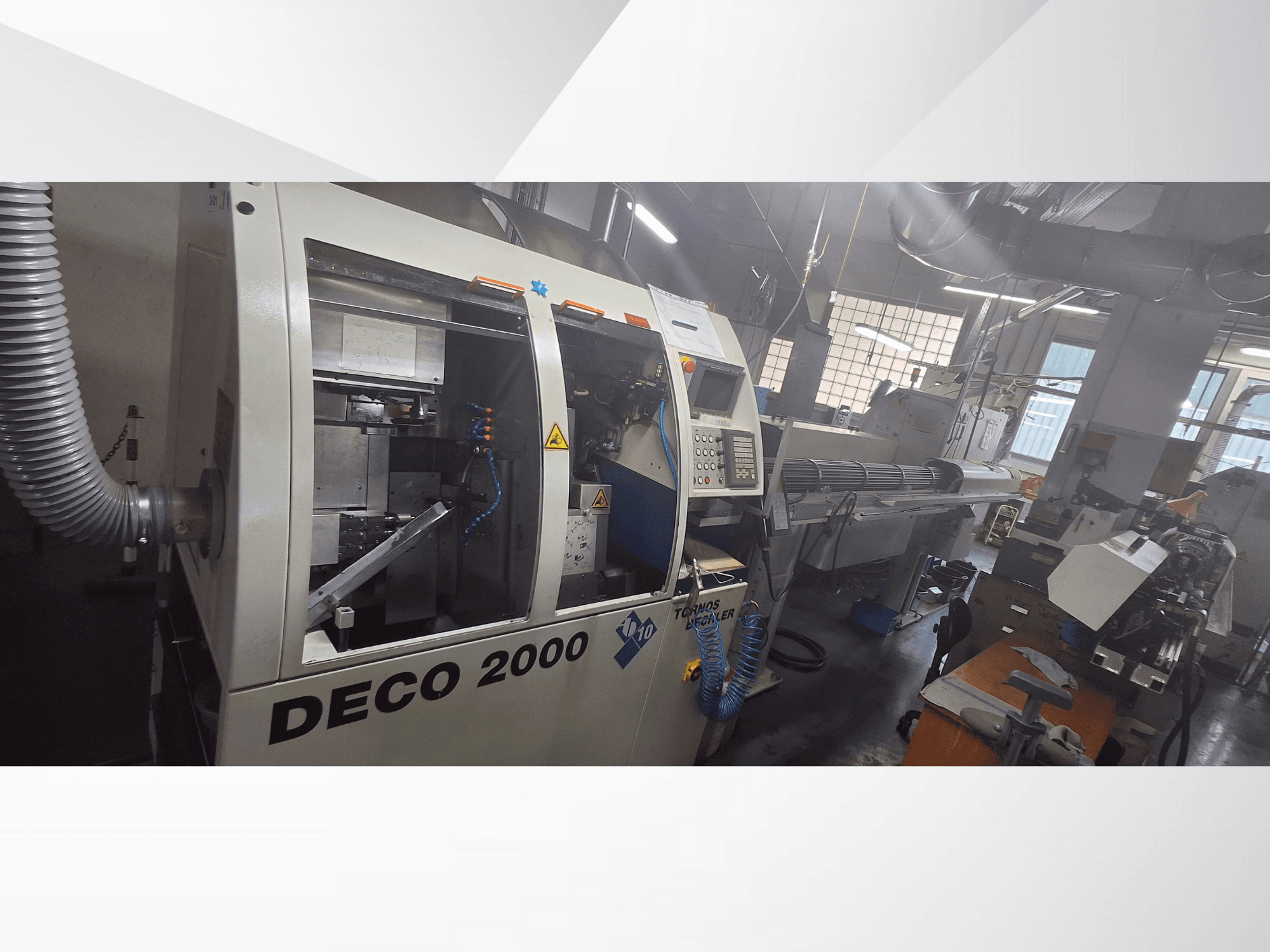 Máquina CNC DECO 2000 numa oficina, vista frontal, mostrando os controlos e uma configuração de peça longa à direita.
