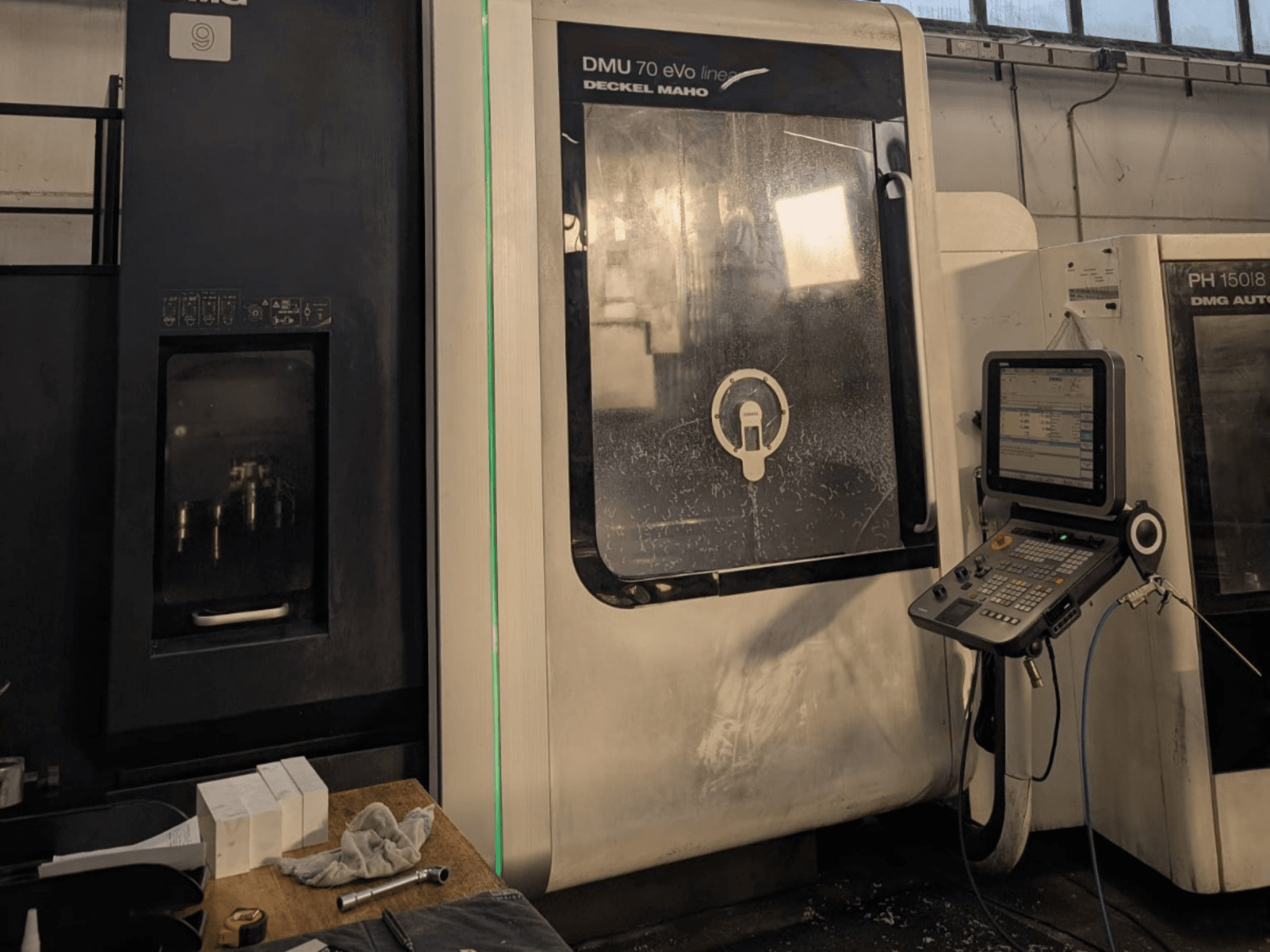 DMG DECKEL MAHO DMU 70 EVO Centro de maquinação vertical linear, vista frontal com painel de controlo, ferramentas e espaço de trabalho visíveis.