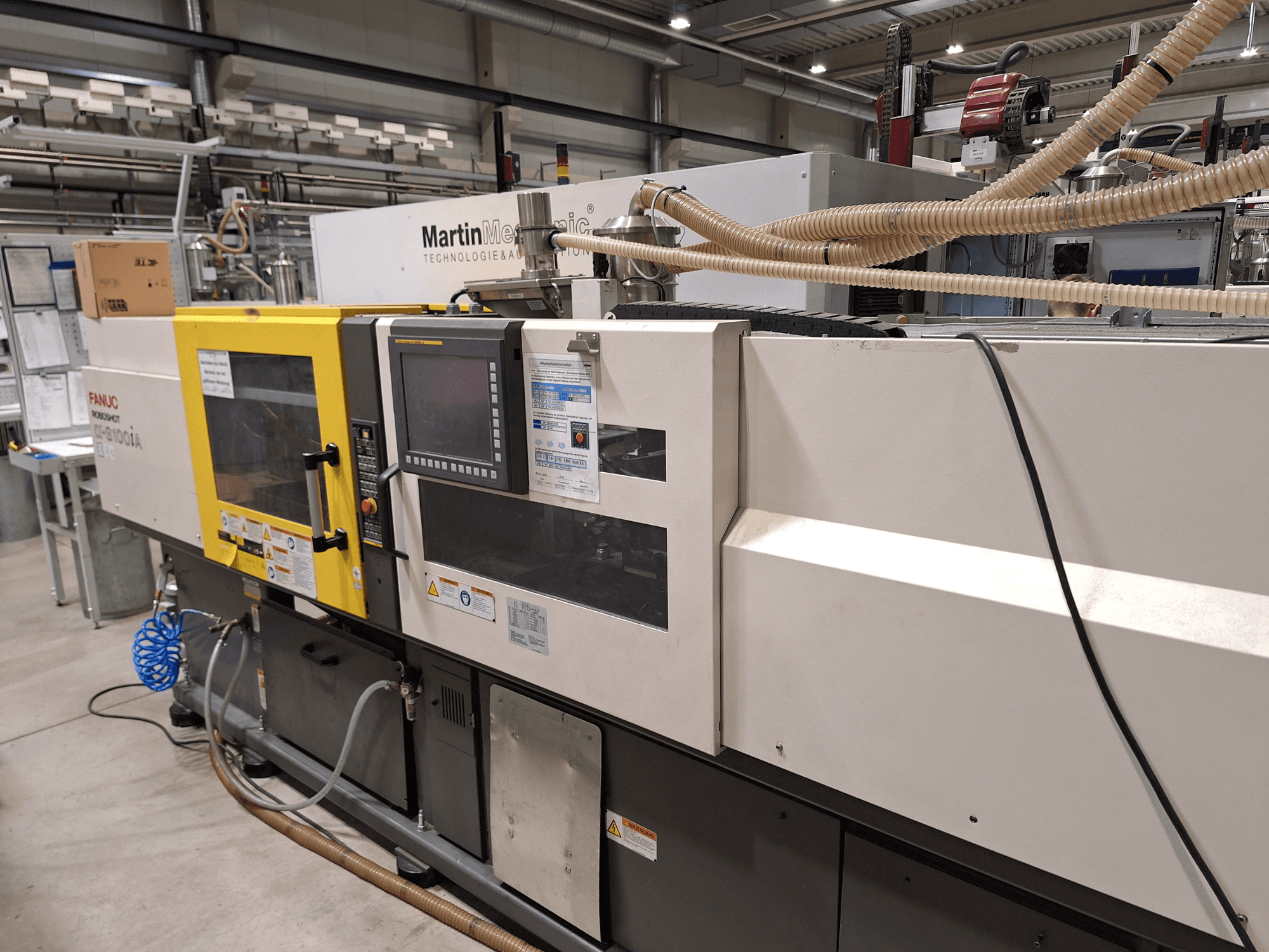 Máquina de moldagem por injeção eléctrica FANUC Roboshot S100iA, vista lateral, equipada com ecrã tátil e etiquetas de segurança.