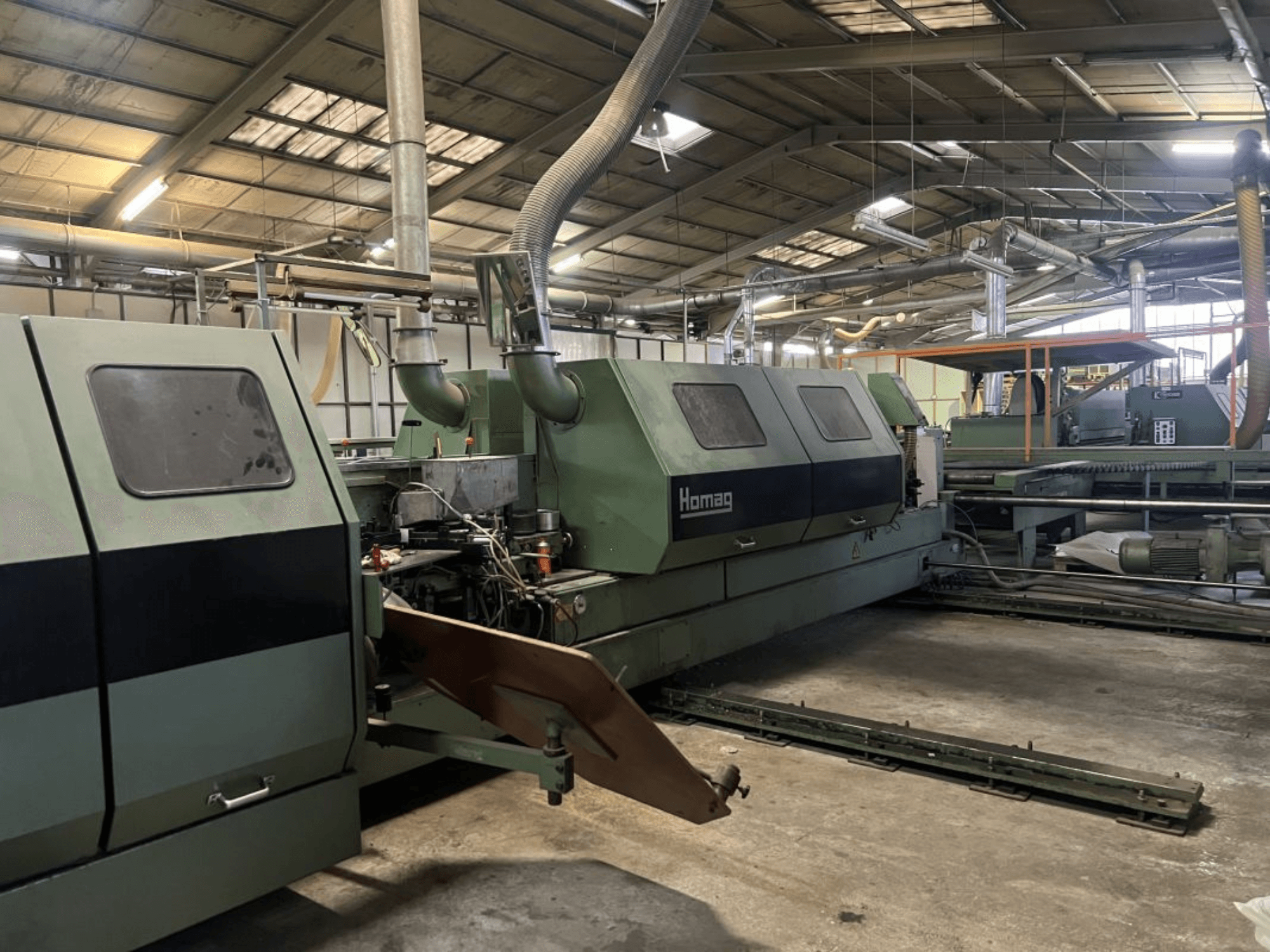 Máquina industrial Homag em verde, vista lateral, com componentes operacionais e painel de controlo visíveis num armazém.