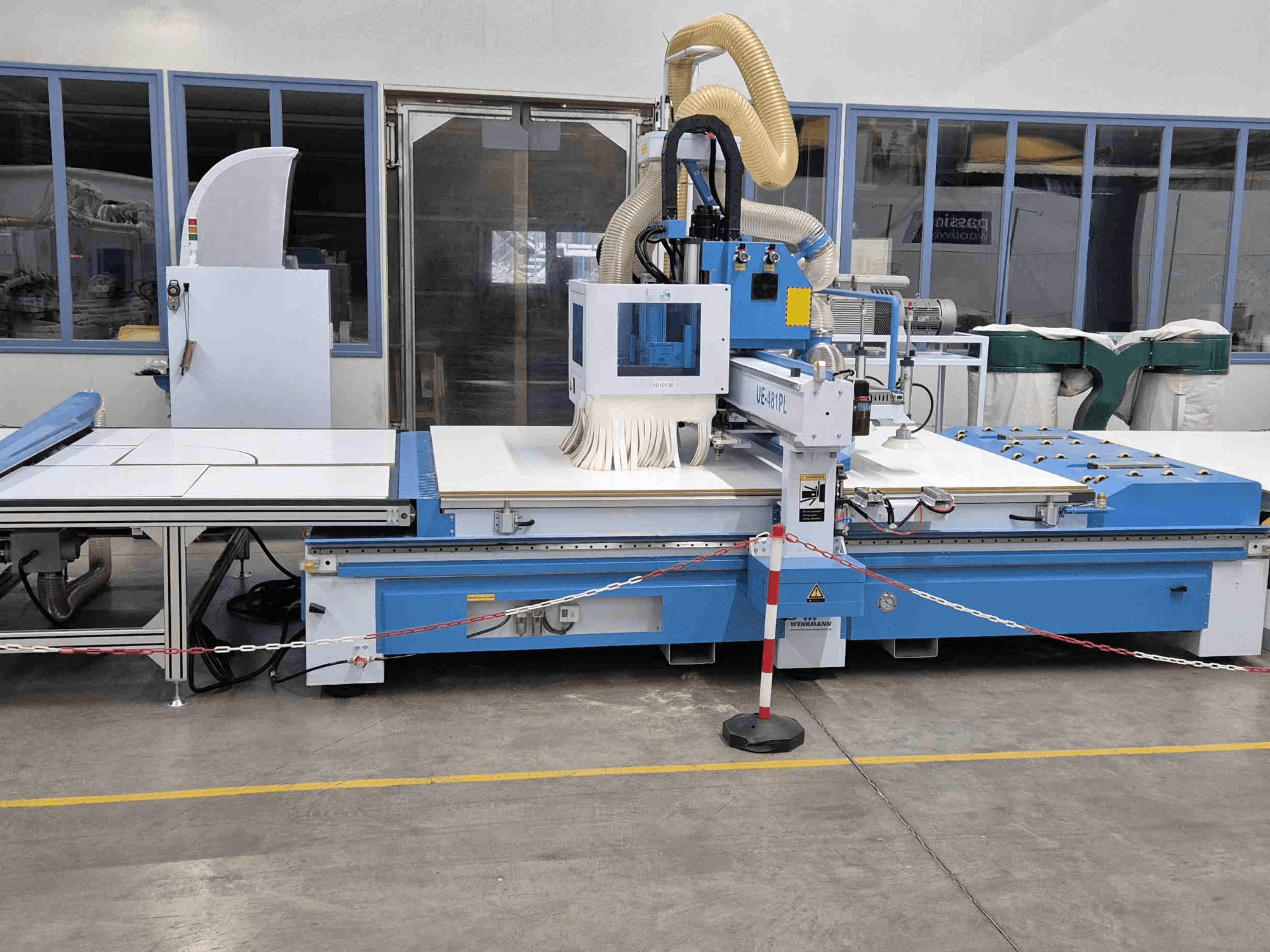 A fresadora CNC azul UE-621PL vista de frente, com uma grande mesa de corte e um sistema de extração de poeiras acoplado.