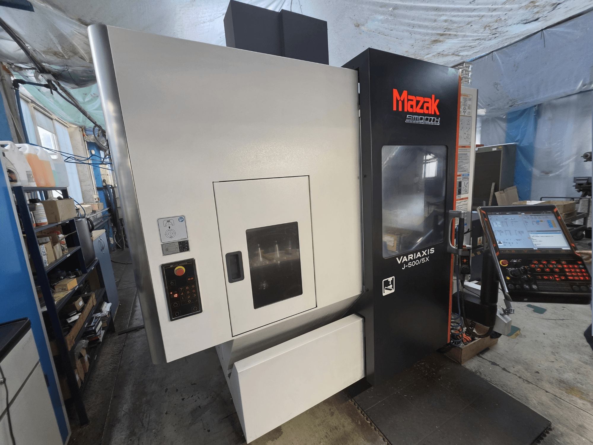 Centro de maquinagem vertical Mazak VARIAXIS J-500/5X visto de frente, com um painel de controlo e uma ampla janela de visualização da área de maquinagem.