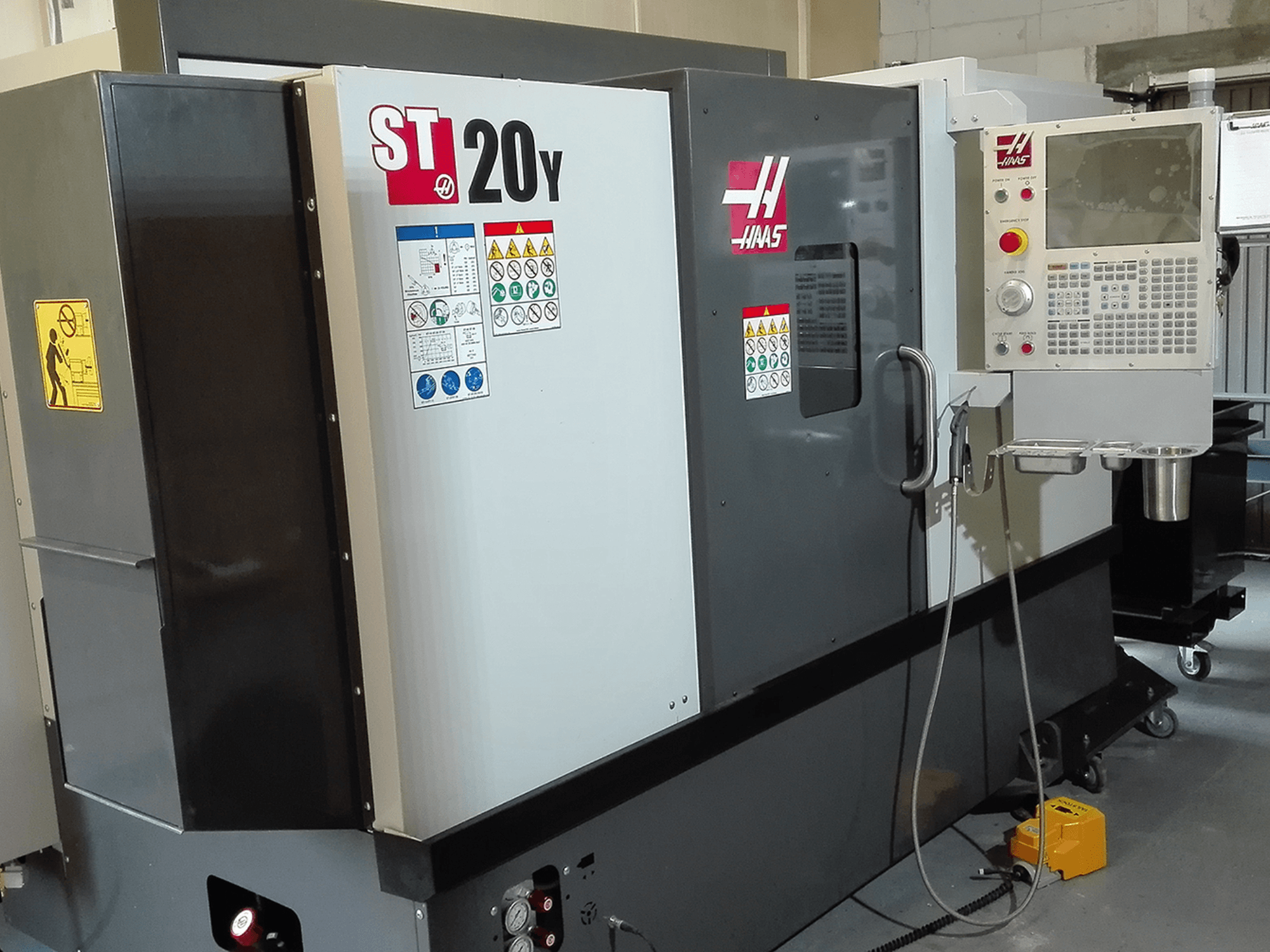 Torno CNC ST20Y da Haas numa vista frontal, com painel de operação, etiquetas de segurança e sistema de refrigeração.