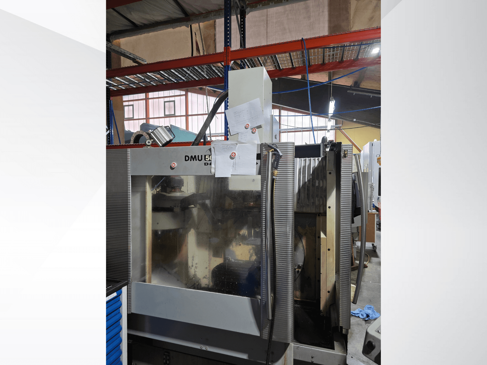 Centro de maquinação CNC de 3 eixos DMU 50 numa oficina, mostrado de frente, exibindo componentes operacionais e documentos anexados.