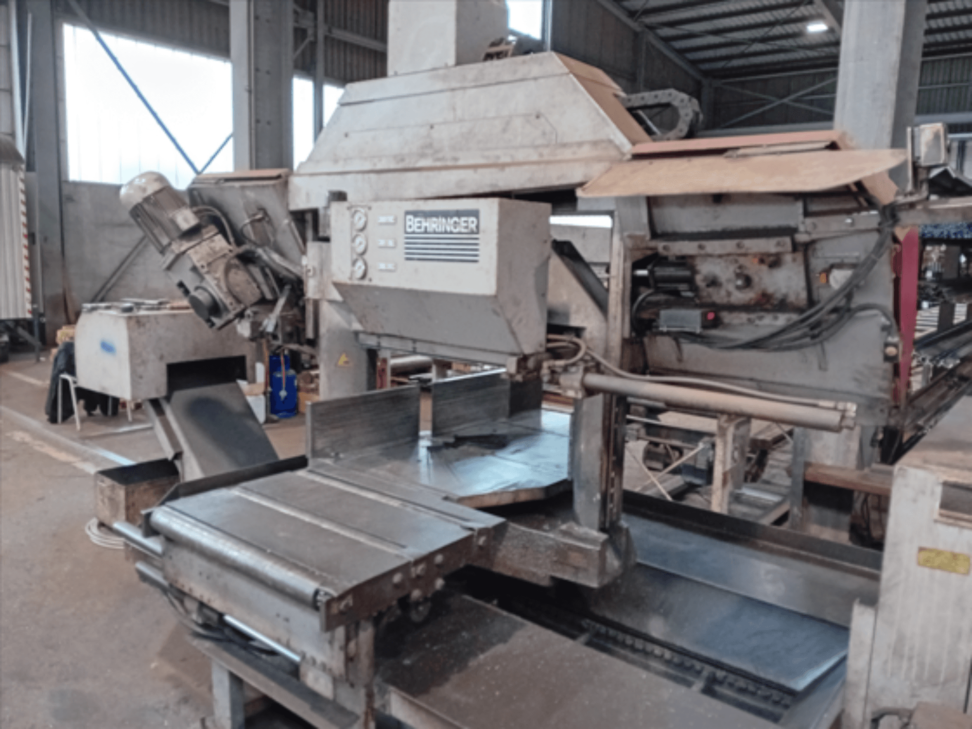 Serra de fita Behringer, vista frontal, com uma lâmina grande, motor e mesa ajustável, ideal para cortar metal numa oficina.