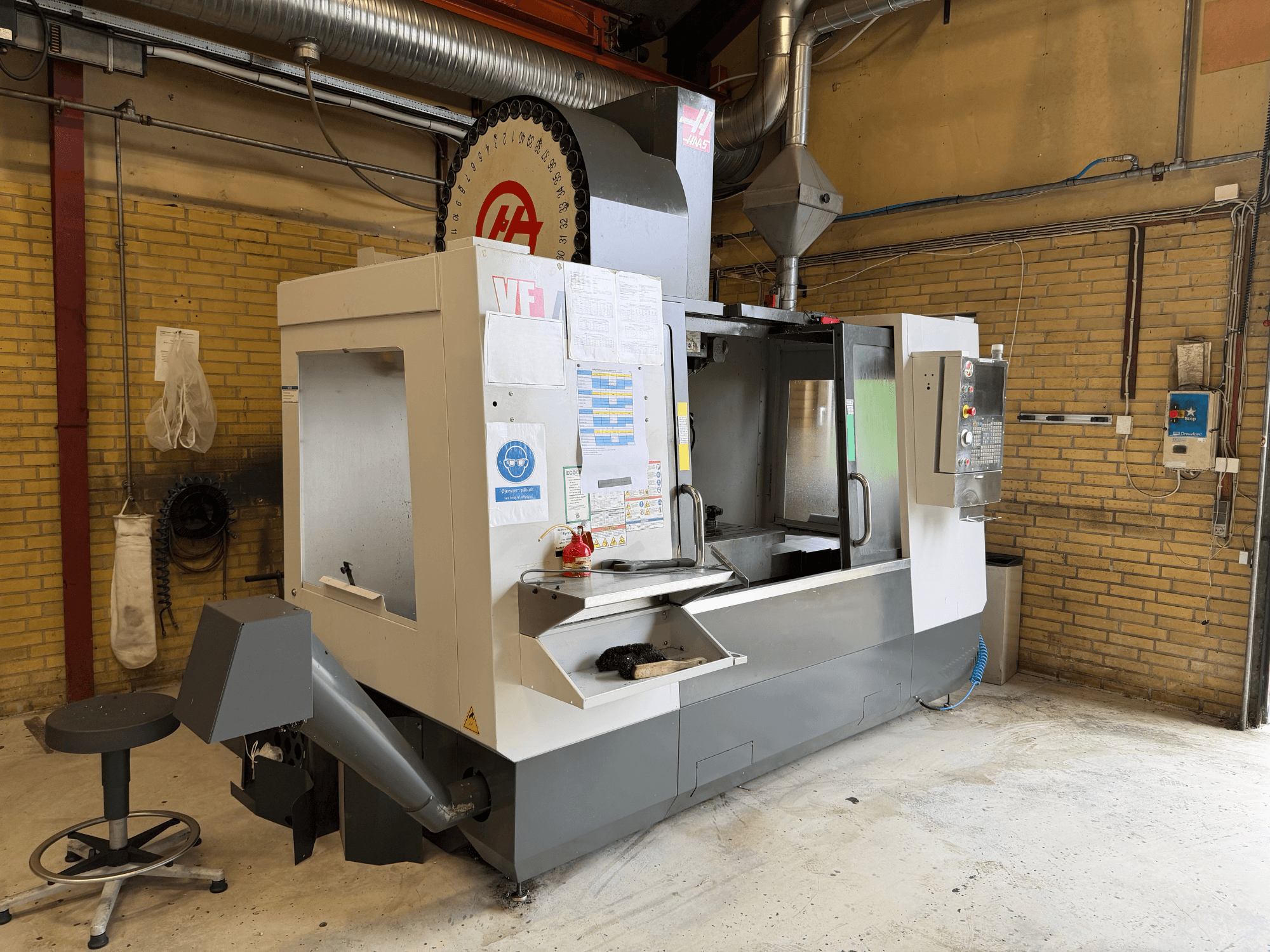 Centro de usinagem vertical HAAS VF-4, vista frontal; apresenta o painel de controlo, o porta-ferramentas e a configuração de produção em segundo plano.