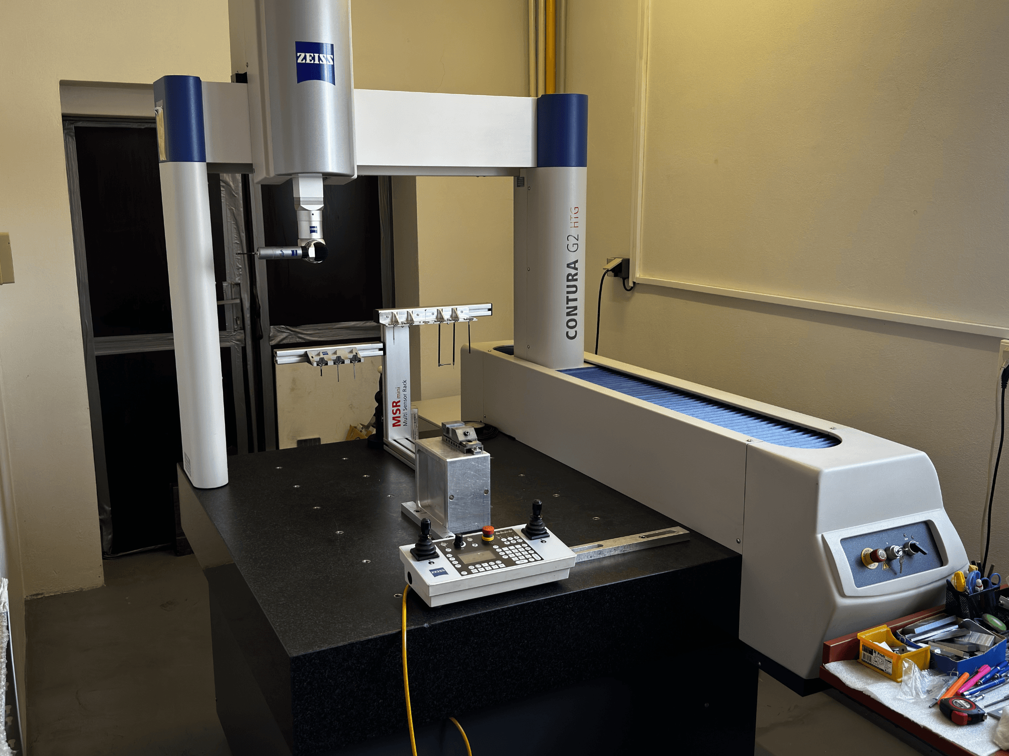 CMM ZEISS Contura G2 num ambiente de laboratório, vista frontal mostrando o braço de medição, o painel de controlo e o espaço de trabalho adjacente.