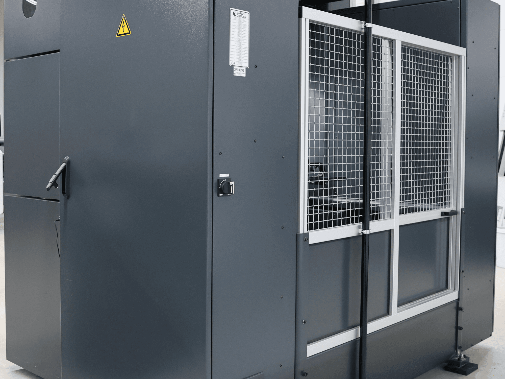 Máquina industrial cinzenta com aviso de segurança, vista frontal mostrando a porta de rede e o painel de controlo, com o modelo identificado.