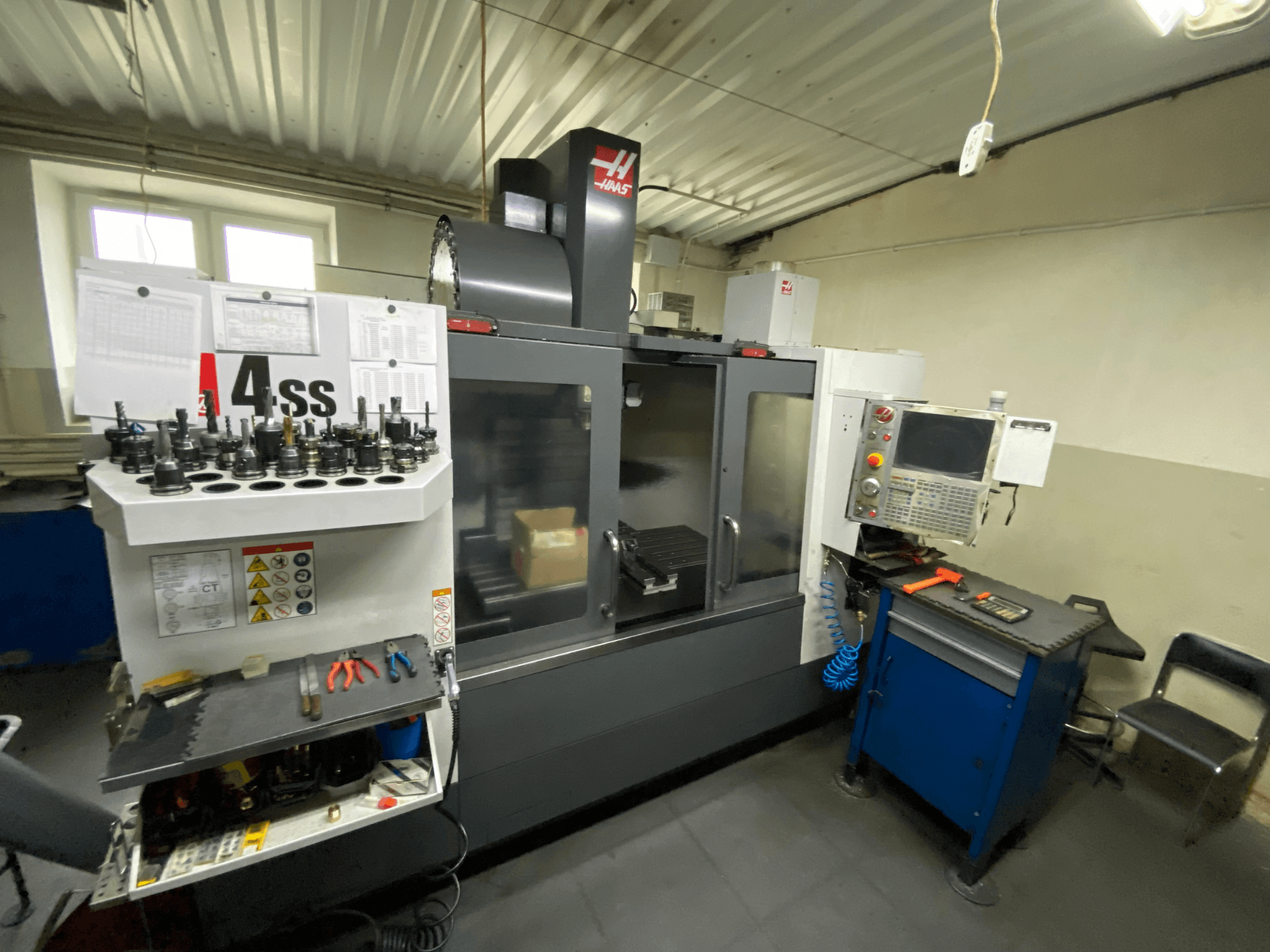Centro de usinagem vertical Haas VF-4SS, vista frontal com porta-ferramentas e painel de controlo. Ferramentas em destaque e área de trabalho visíveis.