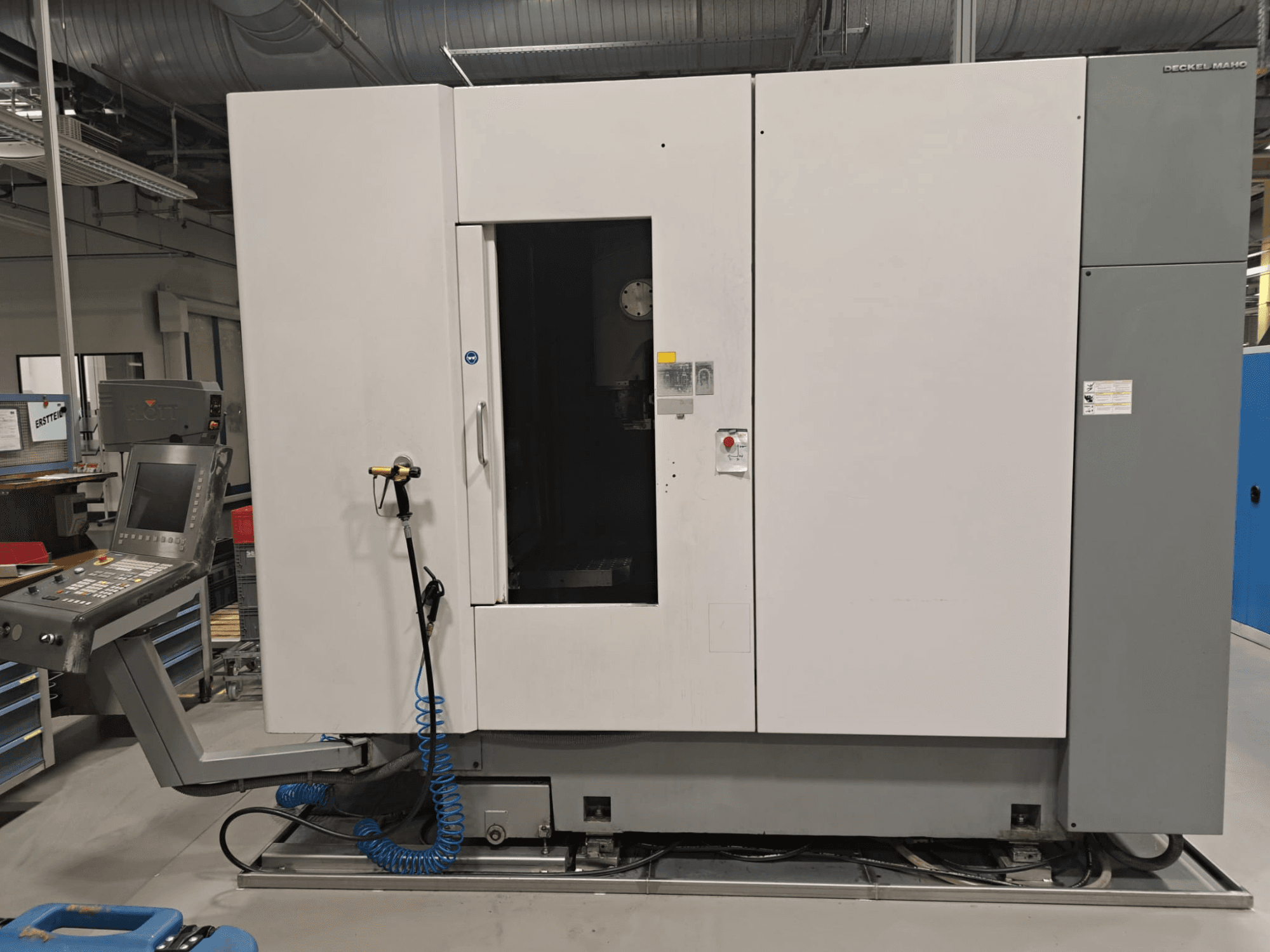 Centro de maquinagem vertical DECKEL MAHO DMP 60V, vista frontal que mostra o painel de controlo e o corpo principal com a porta aberta para facilitar o acesso.