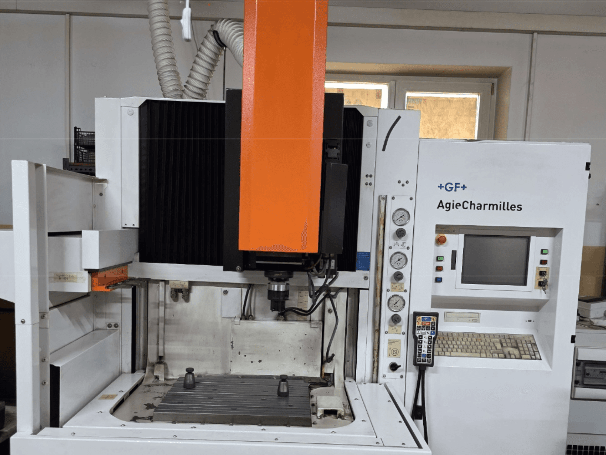 Centro de maquinação AgieCharmilles em vista frontal com um grande fuso laranja, painel de controlo e mesa de trabalho visível.