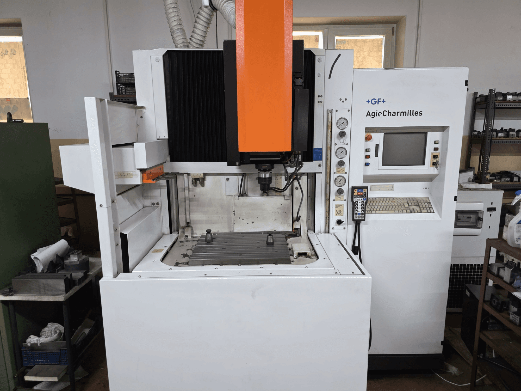 Máquina CNC GF AgieCharmilles, vista frontal com um fuso laranja proeminente, painel de controlo digital e mesa de perfuração montada.