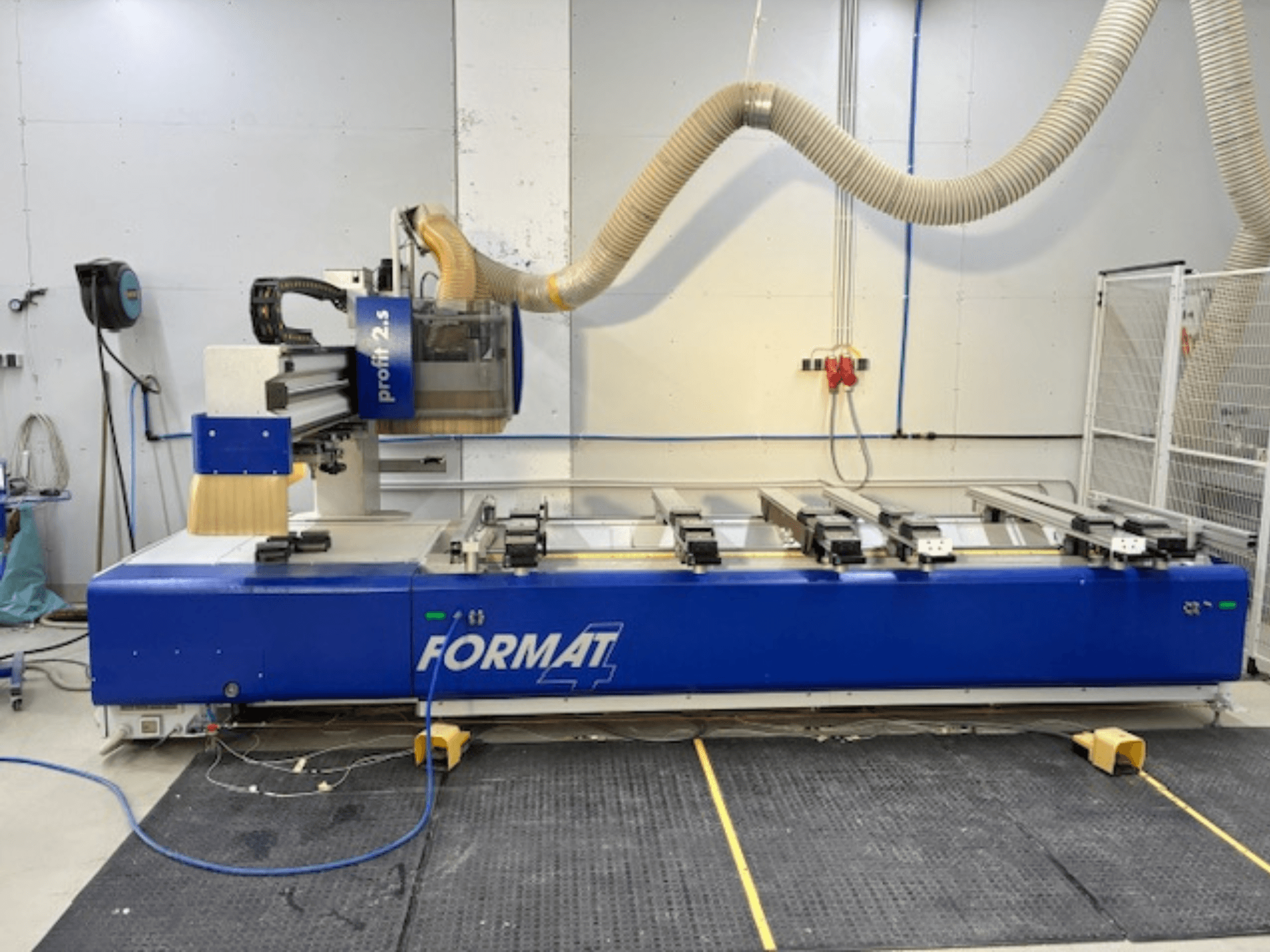 Tupia CNC azul FORMAT 4, modelo Profit 2.5, vista lateral mostrando a área de corte e o sistema de extração de poeiras, sobre um tapete de borracha.