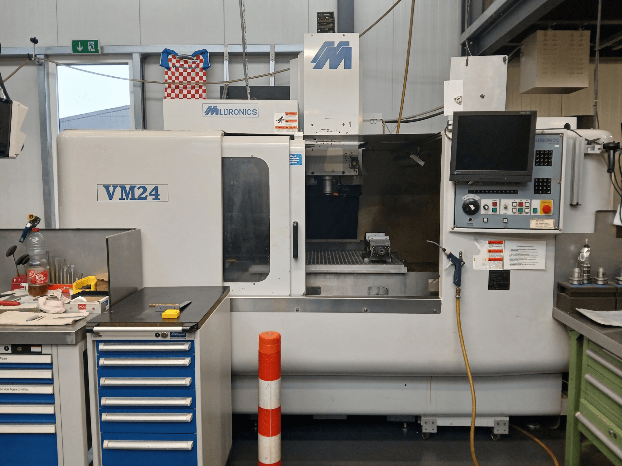 Fresadora CNC Milltronics VM24 mostrada de frente, com um painel de controlo, armazenamento de ferramentas e configuração da área de trabalho.
