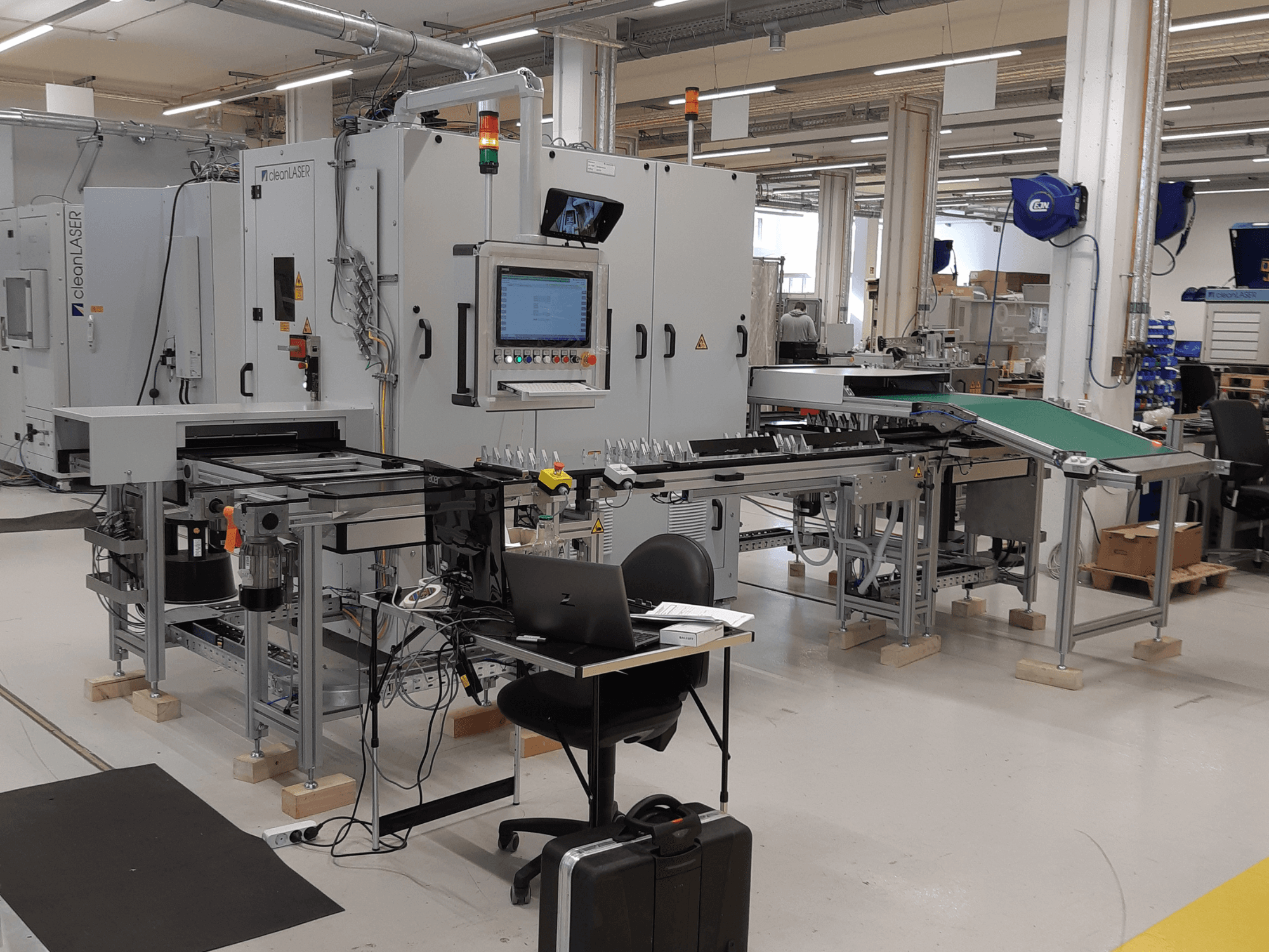 Máquina-ferramenta CLEAN LASER clean CELL 3220, vista frontal que mostra o painel de controlo, o transportador e a configuração da área de trabalho num ambiente fabril.
