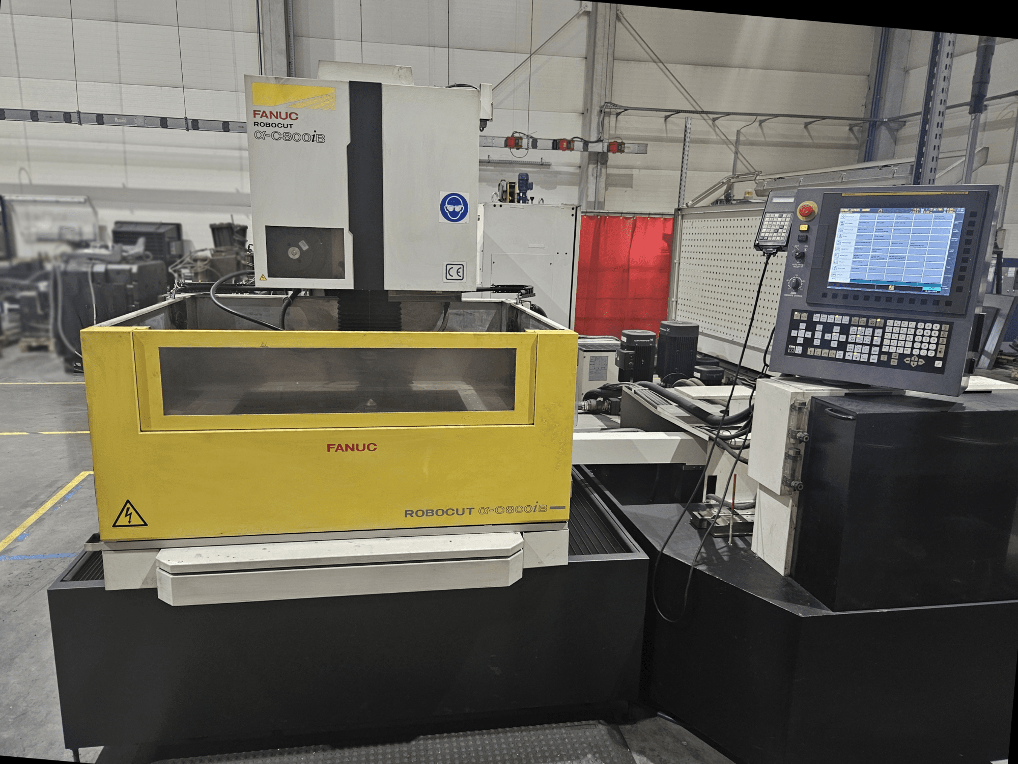 Vista frontal da FANUC Robocut α-C600iB com um corpo de máquina amarelo e cinzento, painel de controlo CNC e visor operacional.