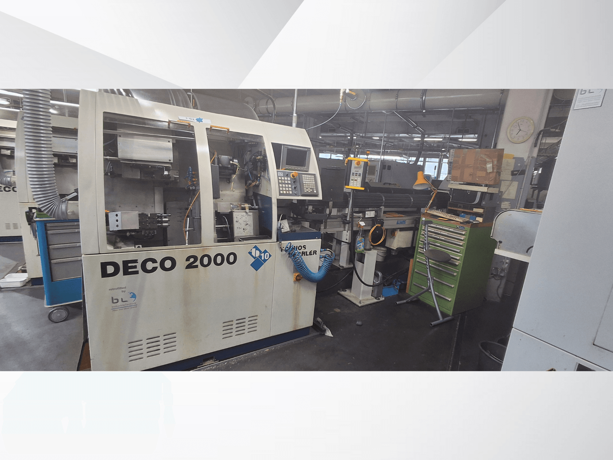 Máquina DECO 2000 vista de frente, com painel de controlo, tubagens e um espaço de trabalho desordenado com ferramentas e caixas.