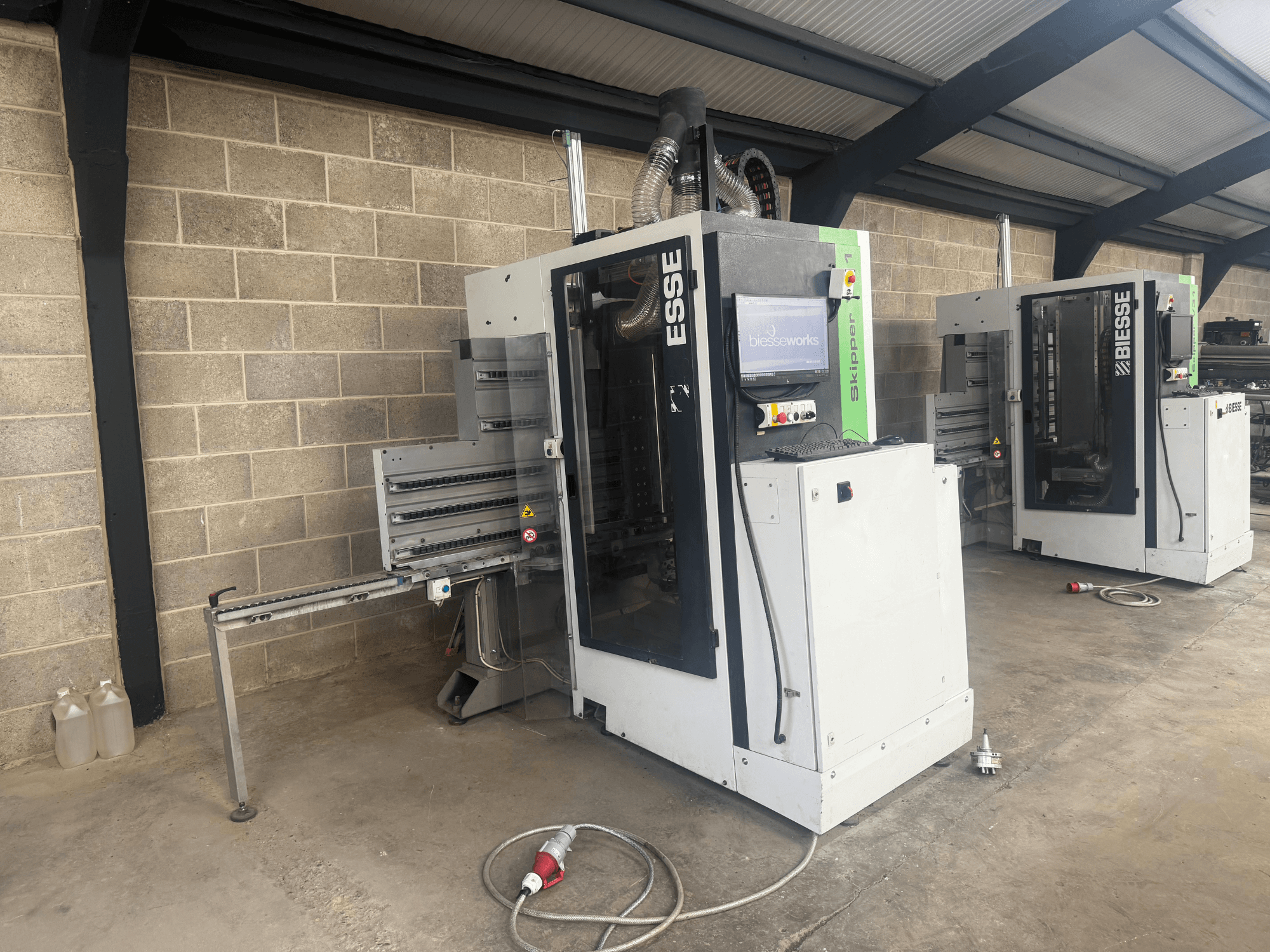 Máquina de furar madeira BIESSE Skipper v31 em vista lateral, com painel de controlo e maquinaria adjacente, colocada numa oficina.