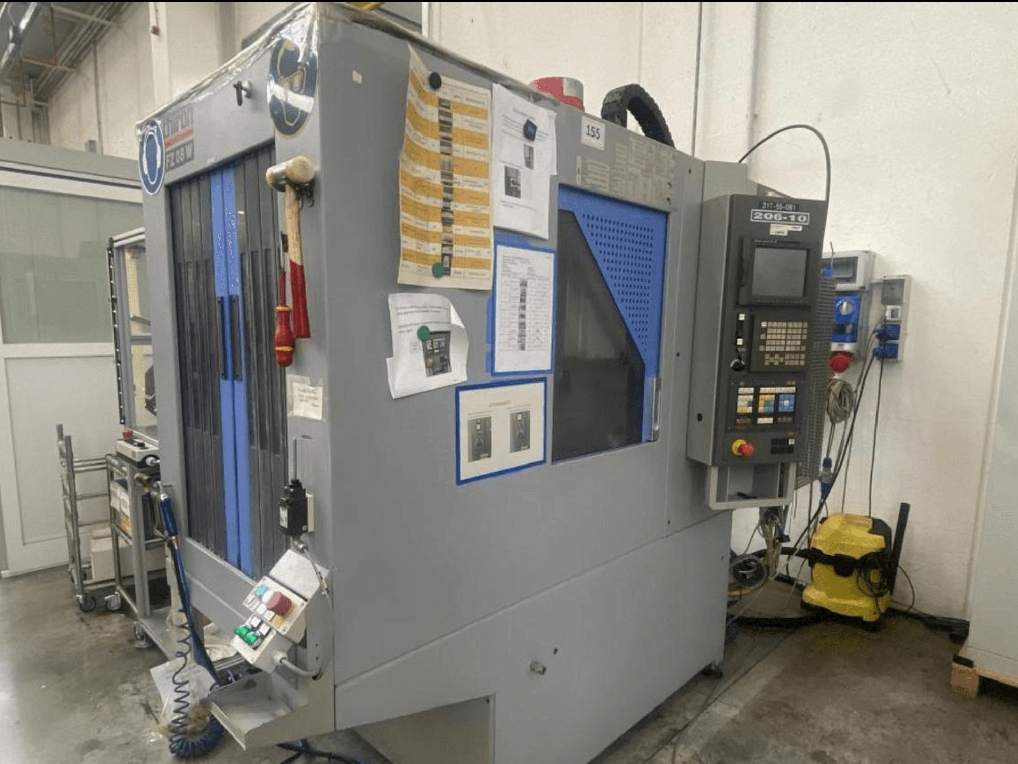 Máquina CNC de Shin Lin, vista frontal, com painel de controlo, botões de funcionamento e instruções de segurança anexas.