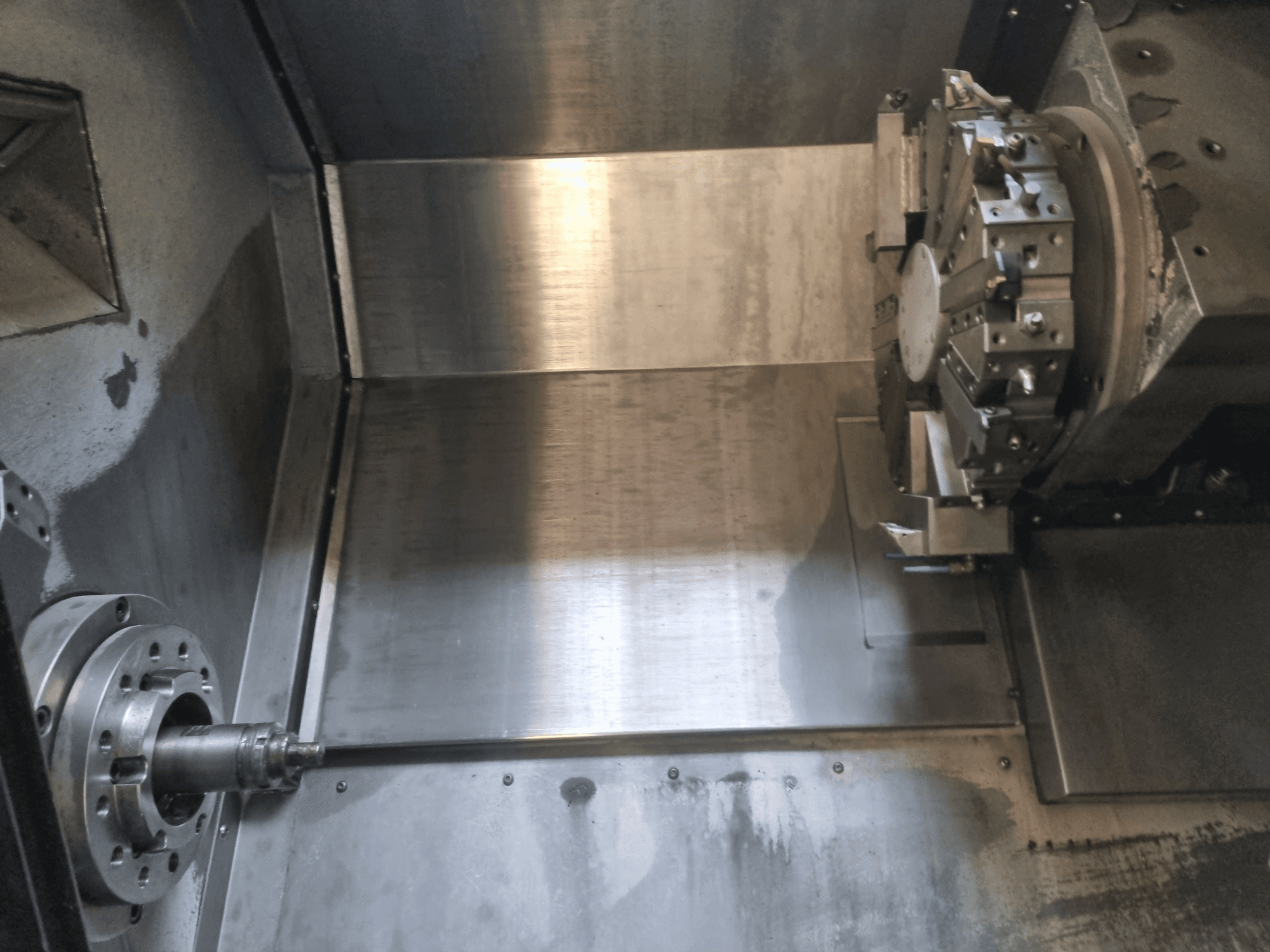 Vista interior de um torno CNC, com um fuso rotativo e uma superfície de trabalho metálica, que mostra a engenharia de precisão industrial.