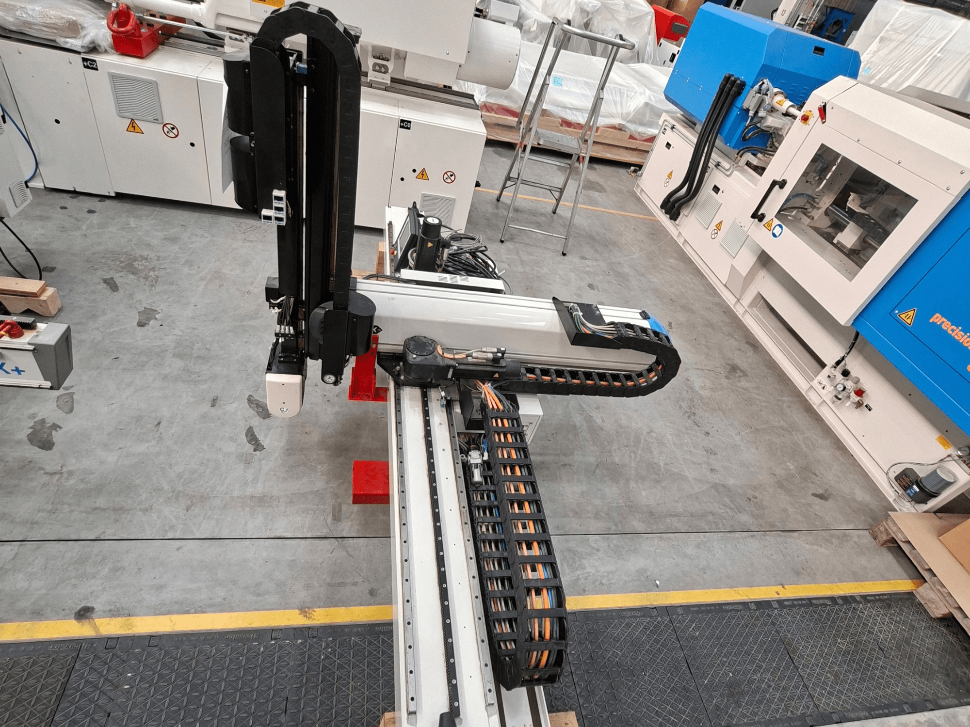 Máquina de transformação de plástico Krauss Maffei LRX150-MC5 vista de cima, mostrando o braço robótico e o canal de cabos no chão de fábrica.