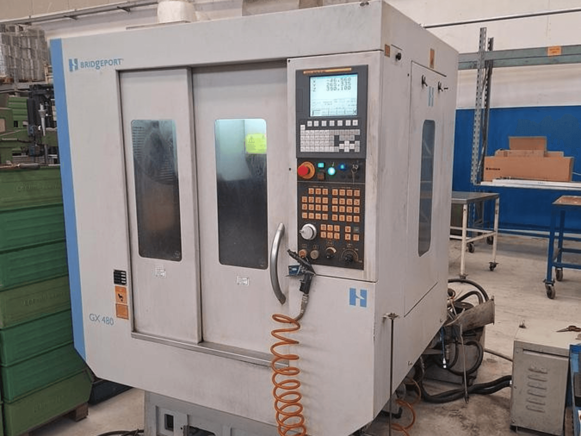 Centro de maquinação vertical Bridgeport GX 480 em vista frontal, com um painel de controlo, portas de vidro duplas e mangueira flexível.