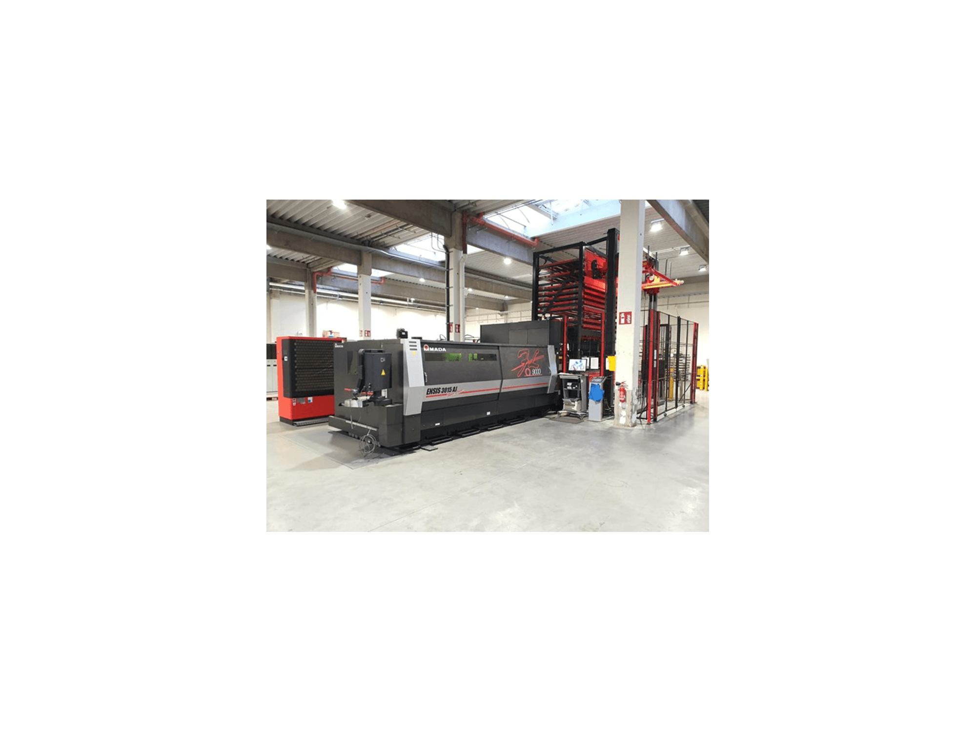 Máquina de corte a laser Amada ENSIS 3015 Aj, vista de frente, numa espaçosa oficina industrial com prateleiras de metal.