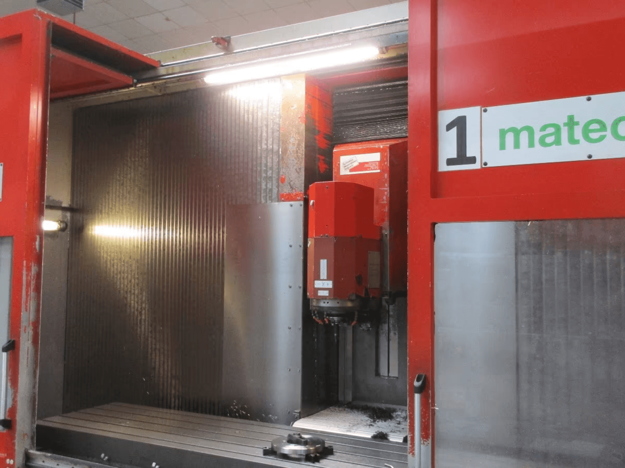 Vista frontal do Centro de Maquinação Vertical CNC Matec 30 HV com ferramenta de corte visível, superfície metálica e detalhes do interior da máquina.