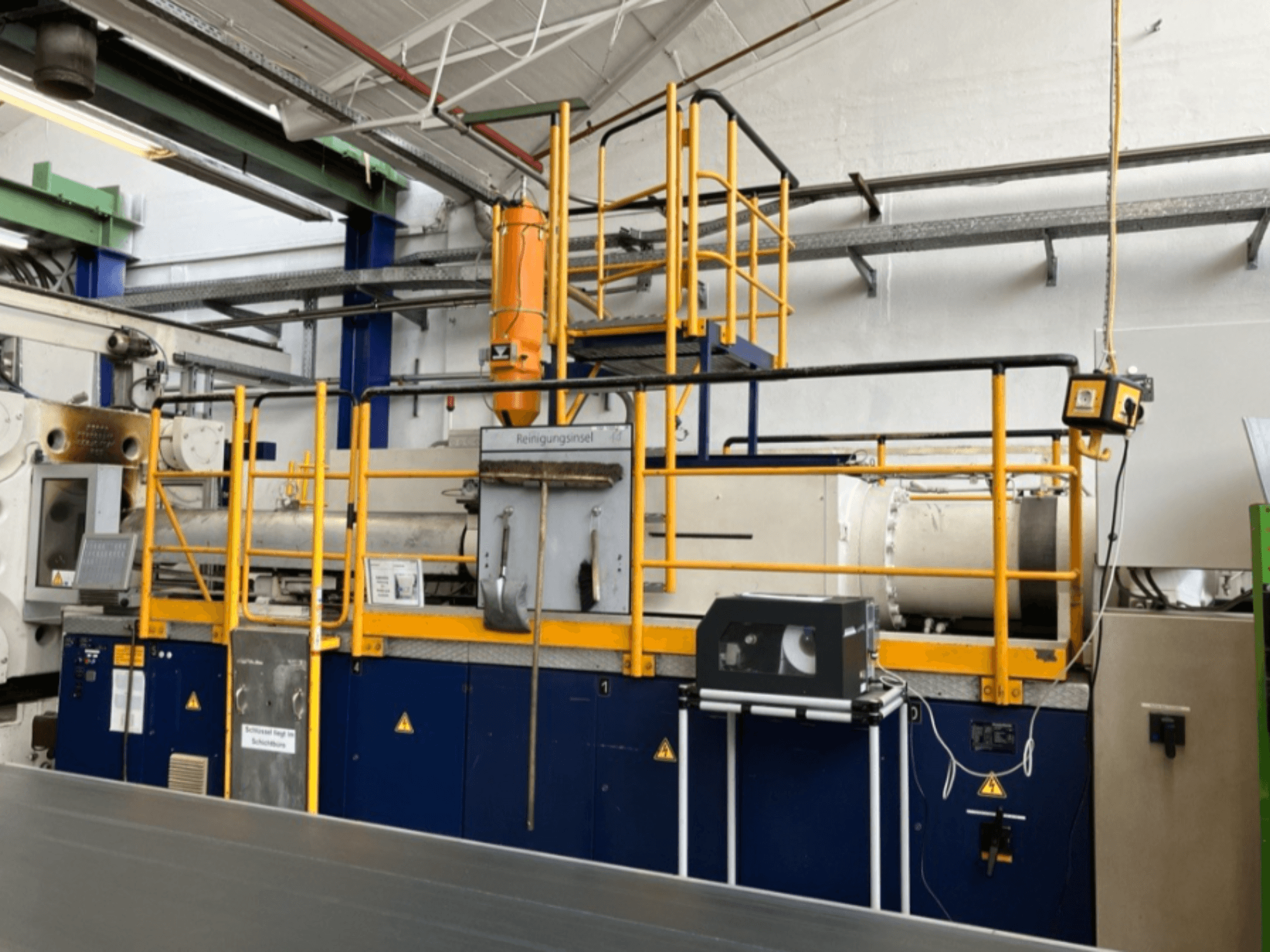 Máquina de moldagem por injeção hidráulica Krauss Maffei 1000-8000 M, vista lateral com grade de segurança e painel de controlo visíveis.