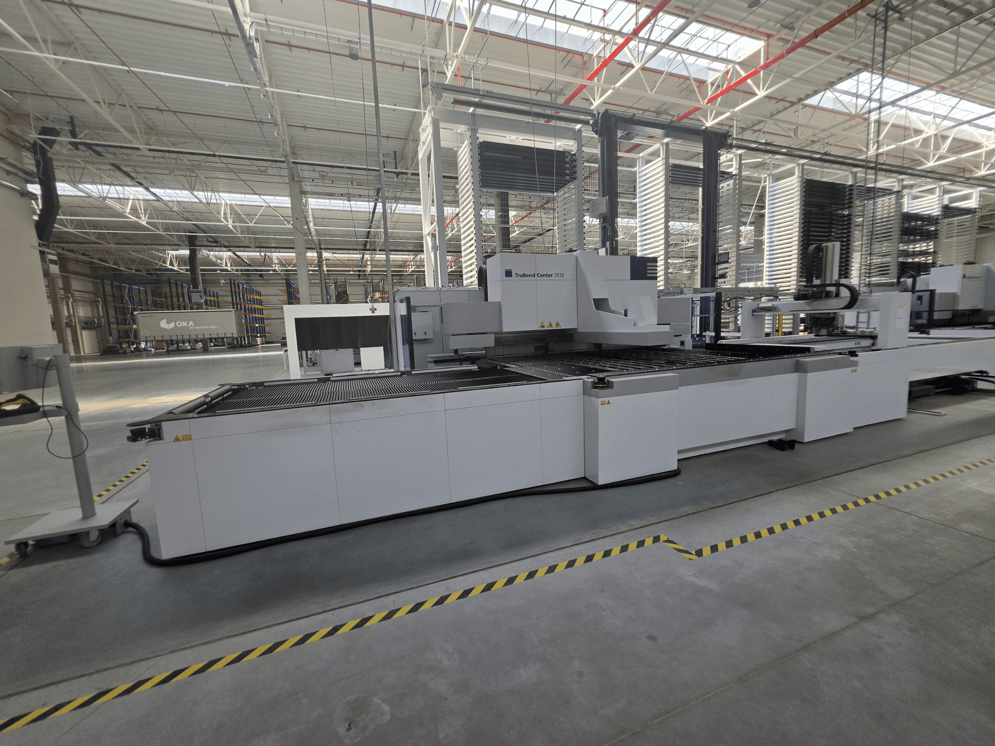 Máquina de dobragem TRUMPF TruBend Center 7030, vista lateral, mostrando a área de trabalho e os comandos numa oficina espaçosa.