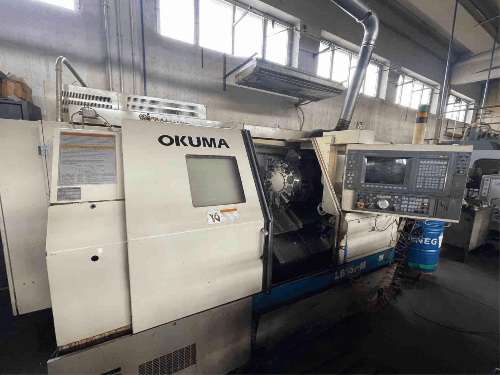 Torneiro horizontal Okuma LB15i-M, vista frontal; possui painel de controlo e área de ferramentas de corte com indicadores detalhados.