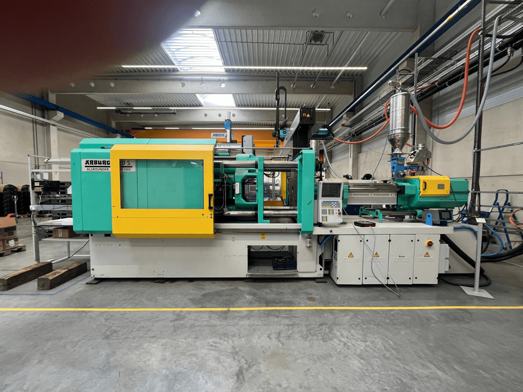 Máquina de moldagem por injeção de plástico ARBURG Allrounder 370S, vista lateral, com caixa verde e amarela, interface de comando visível.