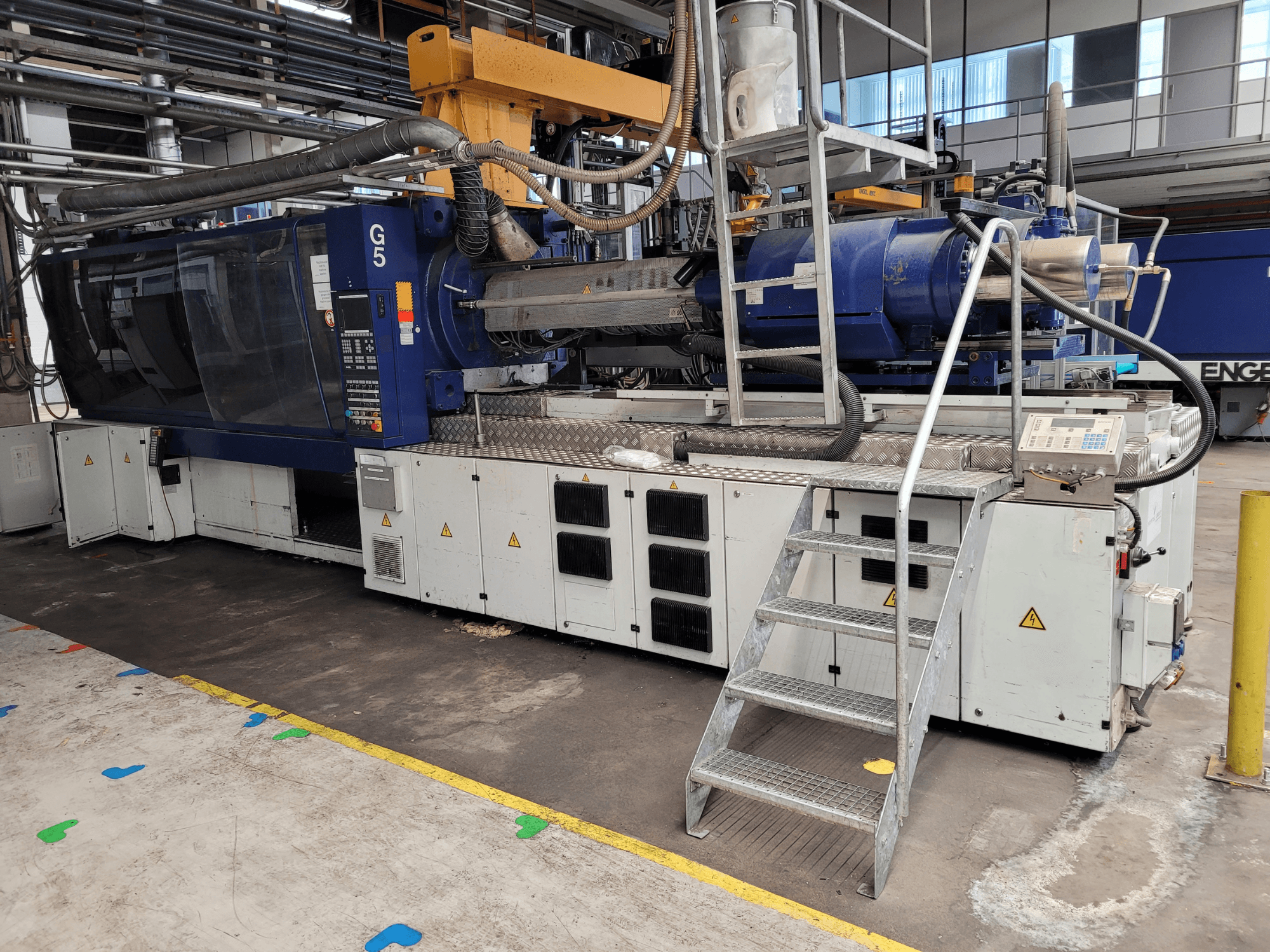 Máquina de moldagem por injeção G5, vista lateral, com painel de controlo, escadote e superfície de trabalho em aço inoxidável visíveis.