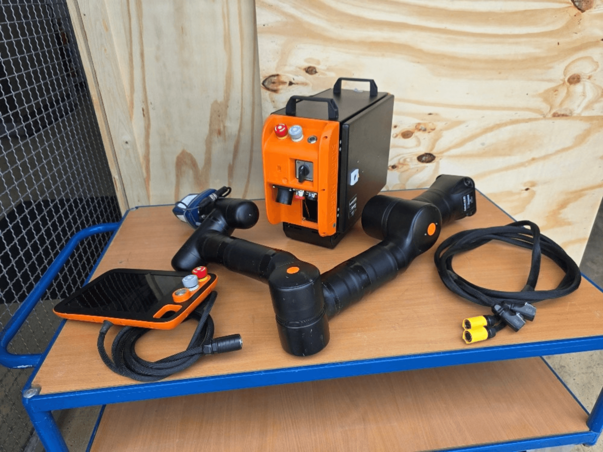 Robô colaborativo KASSOW ROBOTS KR810, vista frontal, incluindo o controlador, os cabos e os conectores sobre uma mesa de madeira.