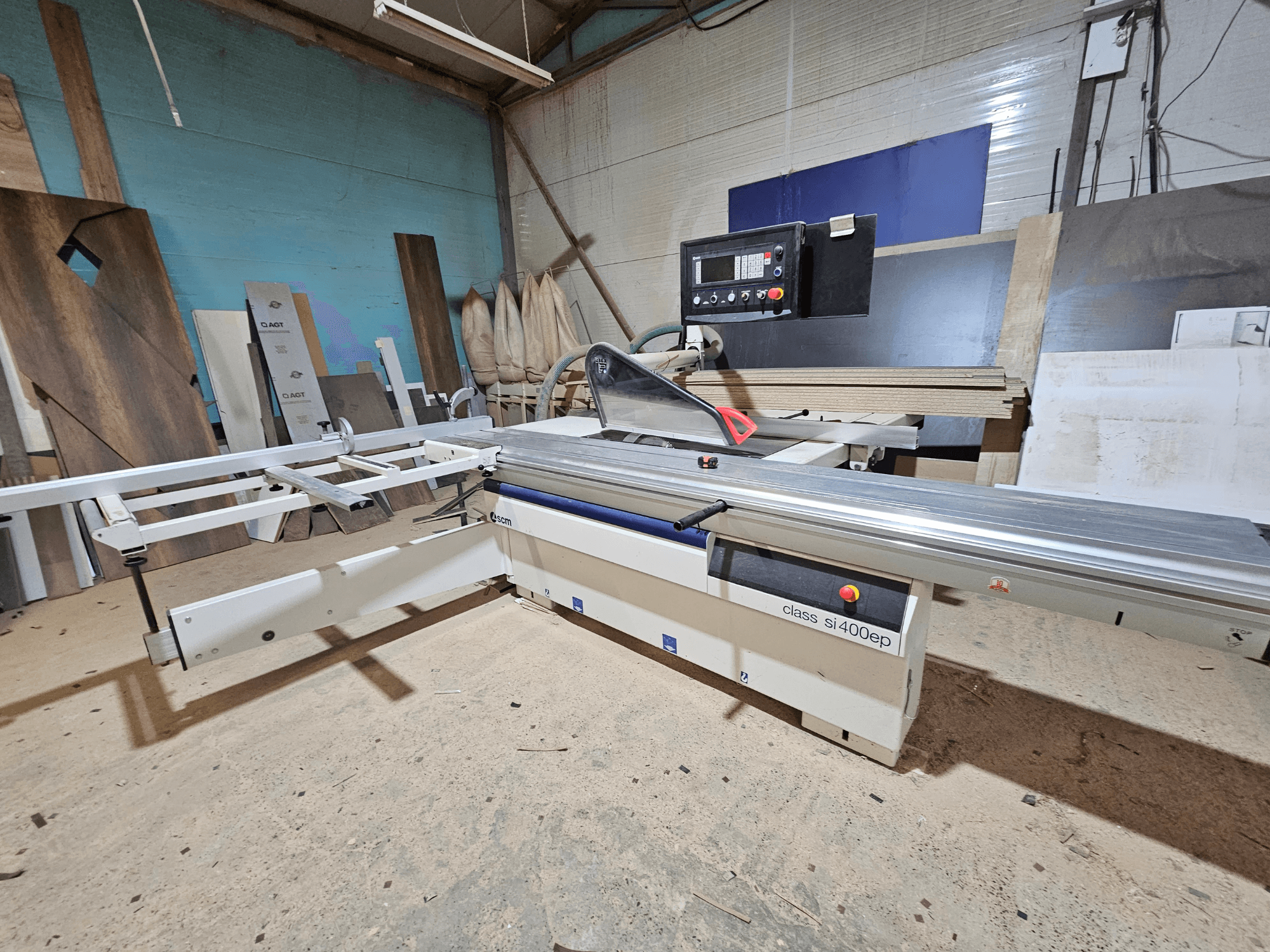 Serra de painel da classe SI400EP, vista frontal, com vedação ajustável, colocada no chão arenoso da oficina, rodeada por painéis de madeira.