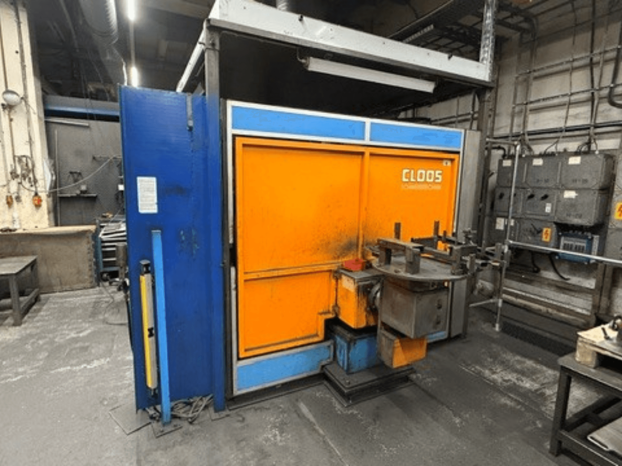 Robô de soldadura CLOOS Romat 320 numa oficina, vista frontal que mostra a estrutura em laranja e azul com o painel de controlo e as ferramentas.