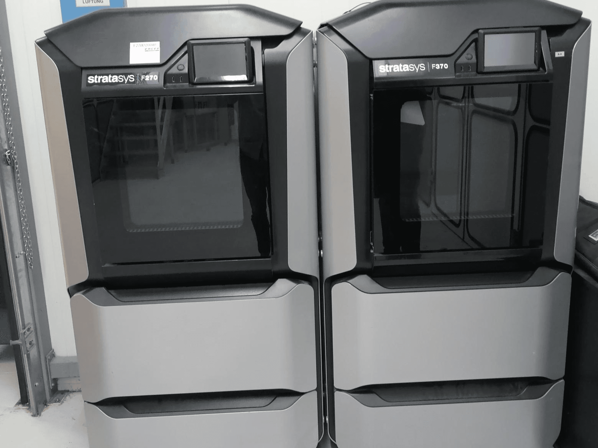 Impressoras 3D Stratasys F370 dual plastic apresentadas numa vista frontal, com um design elegante em preto e prateado com ecrãs de controlo.