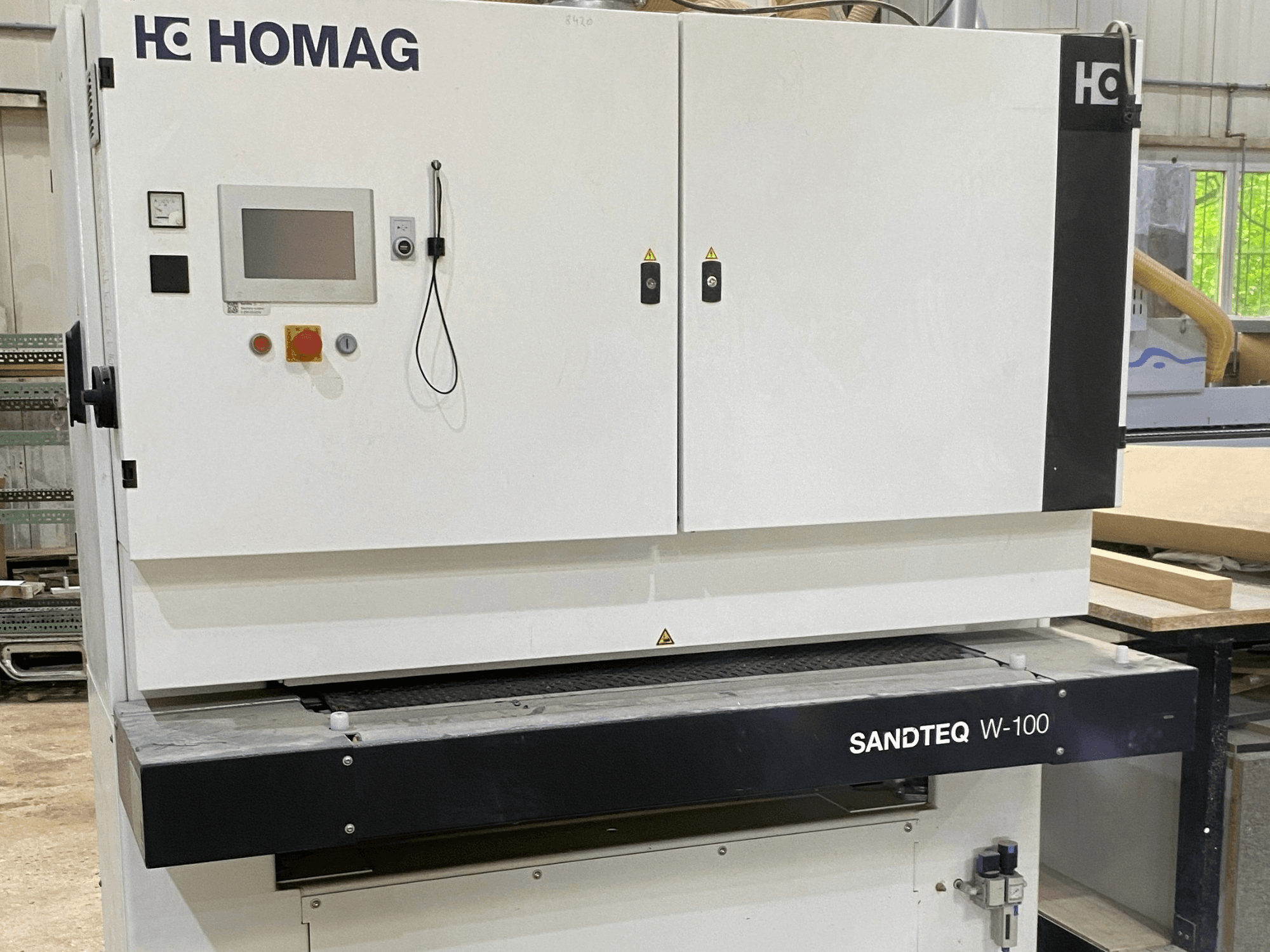 Lixadeira de cinta HOMAG SANDTEQ W-100 numa oficina, mostrando o painel de controlo, a saída de pó e a área da cinta de lixagem. Vista frontal.