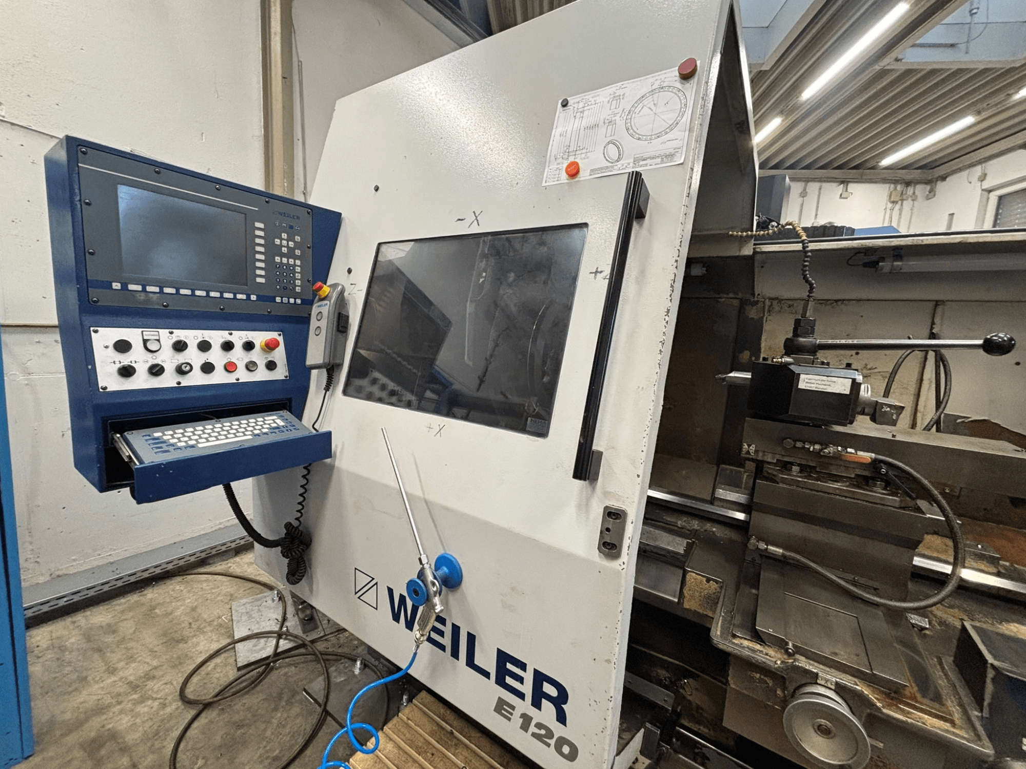 Painel de controlo e interface da máquina CNC Weiler E-120, vista frontal com botões visíveis, ecrã de visualização e componentes de funcionamento.