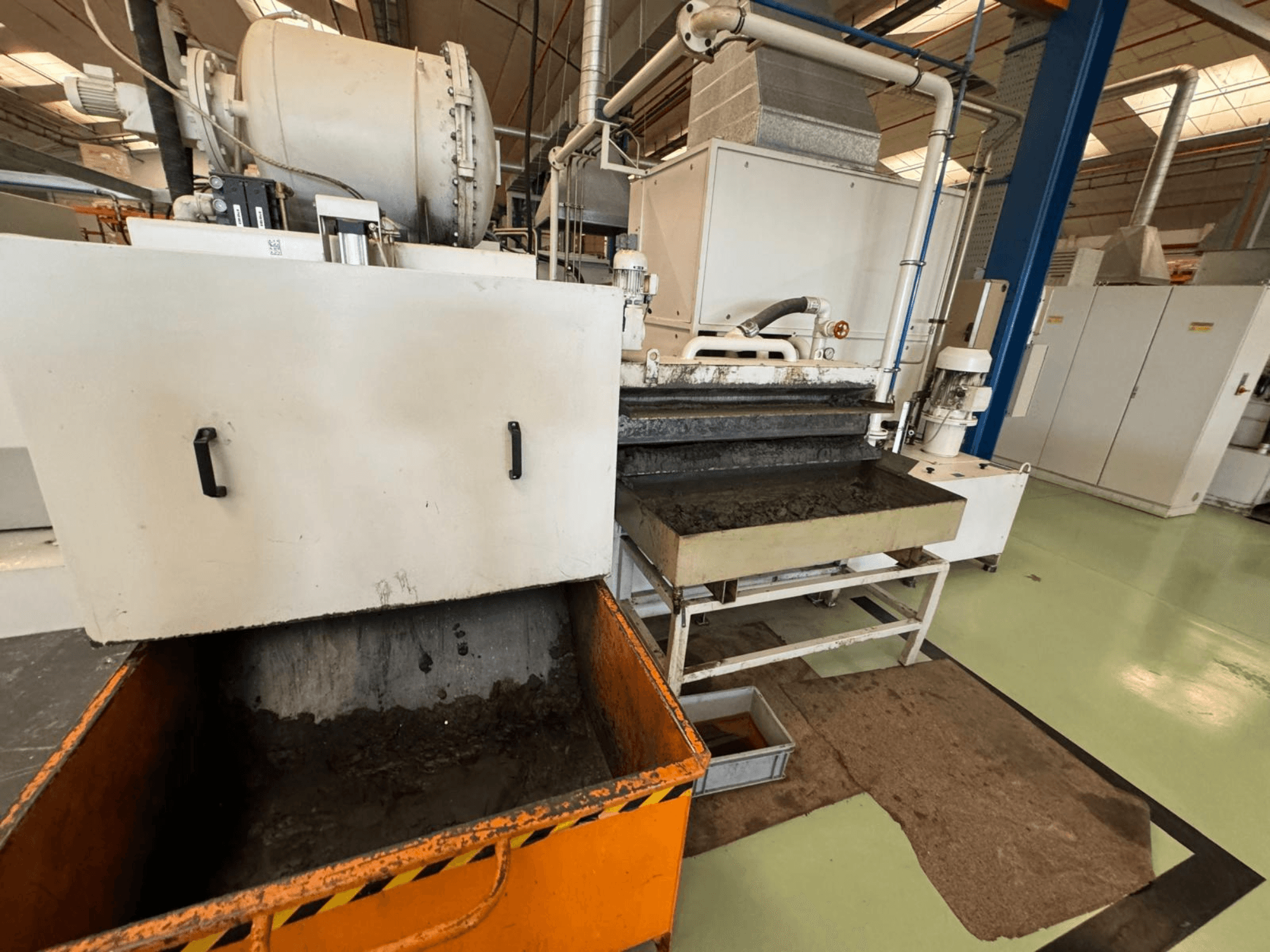 Equipamento de processamento industrial com um caixote do lixo cor de laranja, vista frontal; contém um motor, transportadores e área de manutenção.